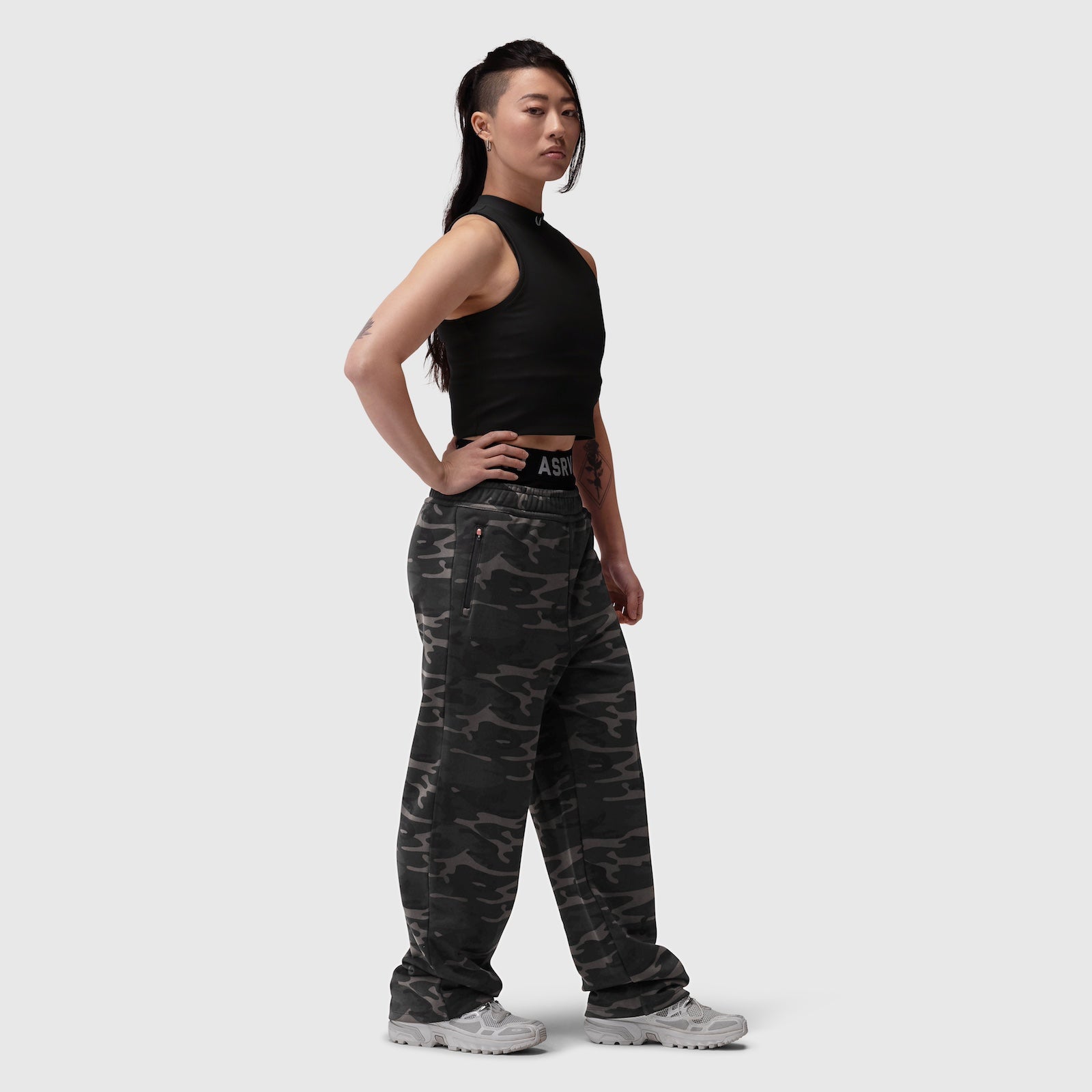 Black ribbed mockneck tank worn with camouflage cargo pants, side view