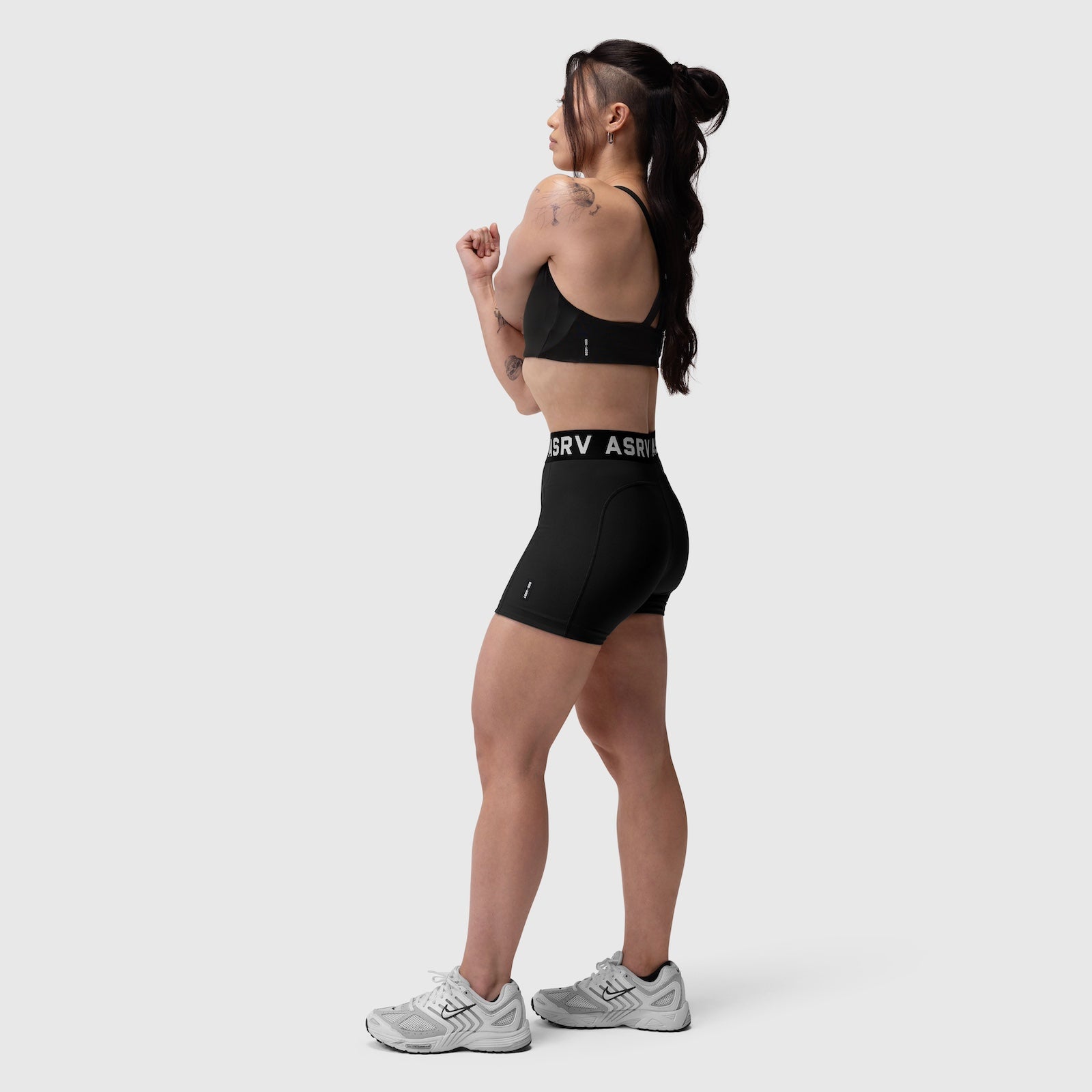 Black LYCRA® Hybrid Sports Bra worn by model in side profile, paired with black shorts