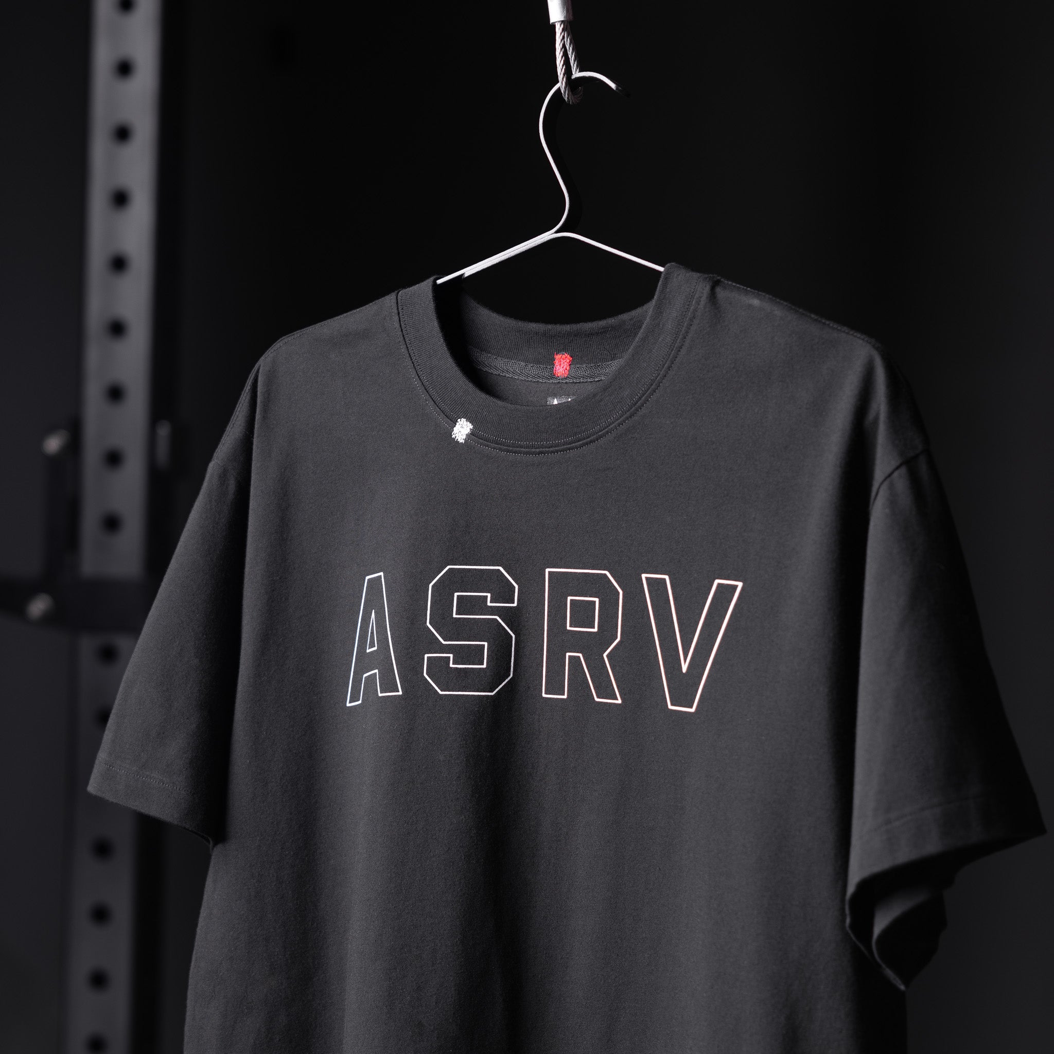 ASRV Tech Essential Relaxed Tee in black with white outline logo, displayed on hanger