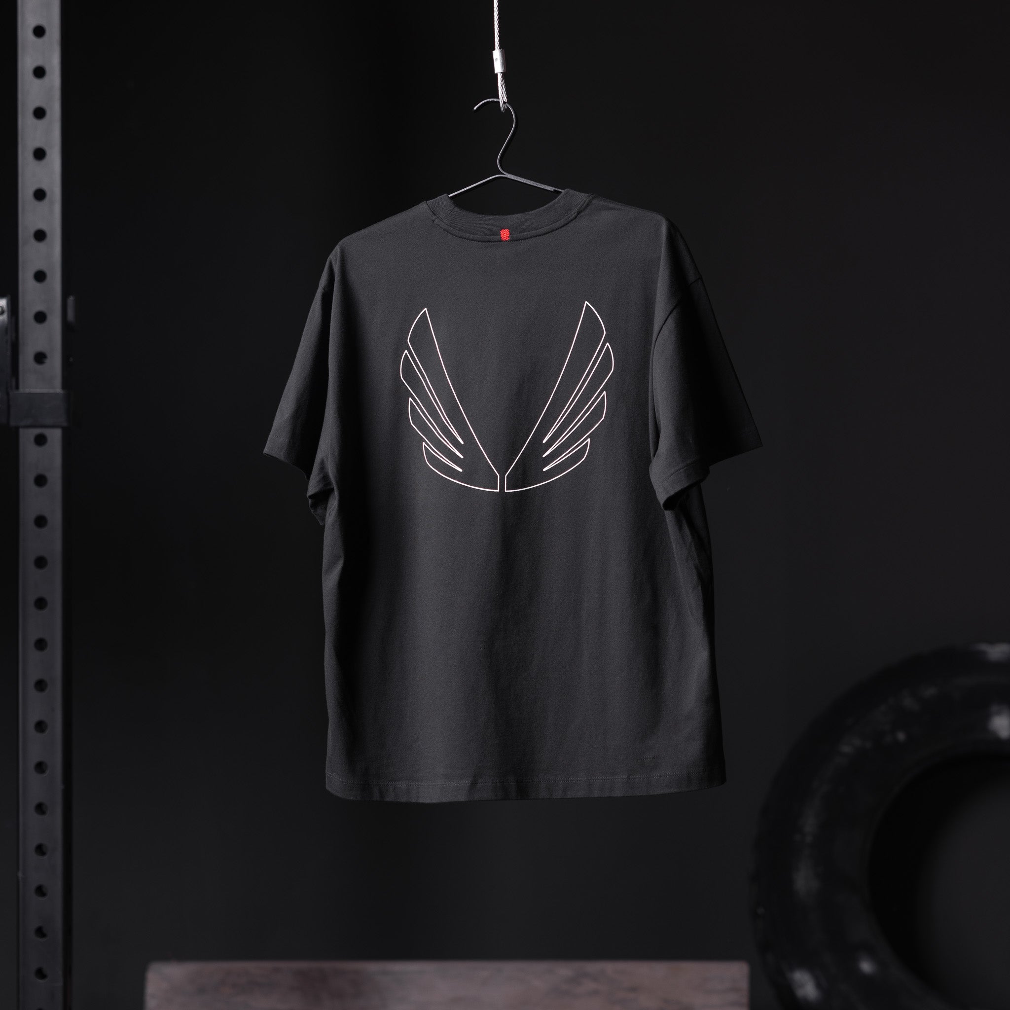Black Tech Essential Relaxed Tee with white outline wing graphic, displayed on hanger
