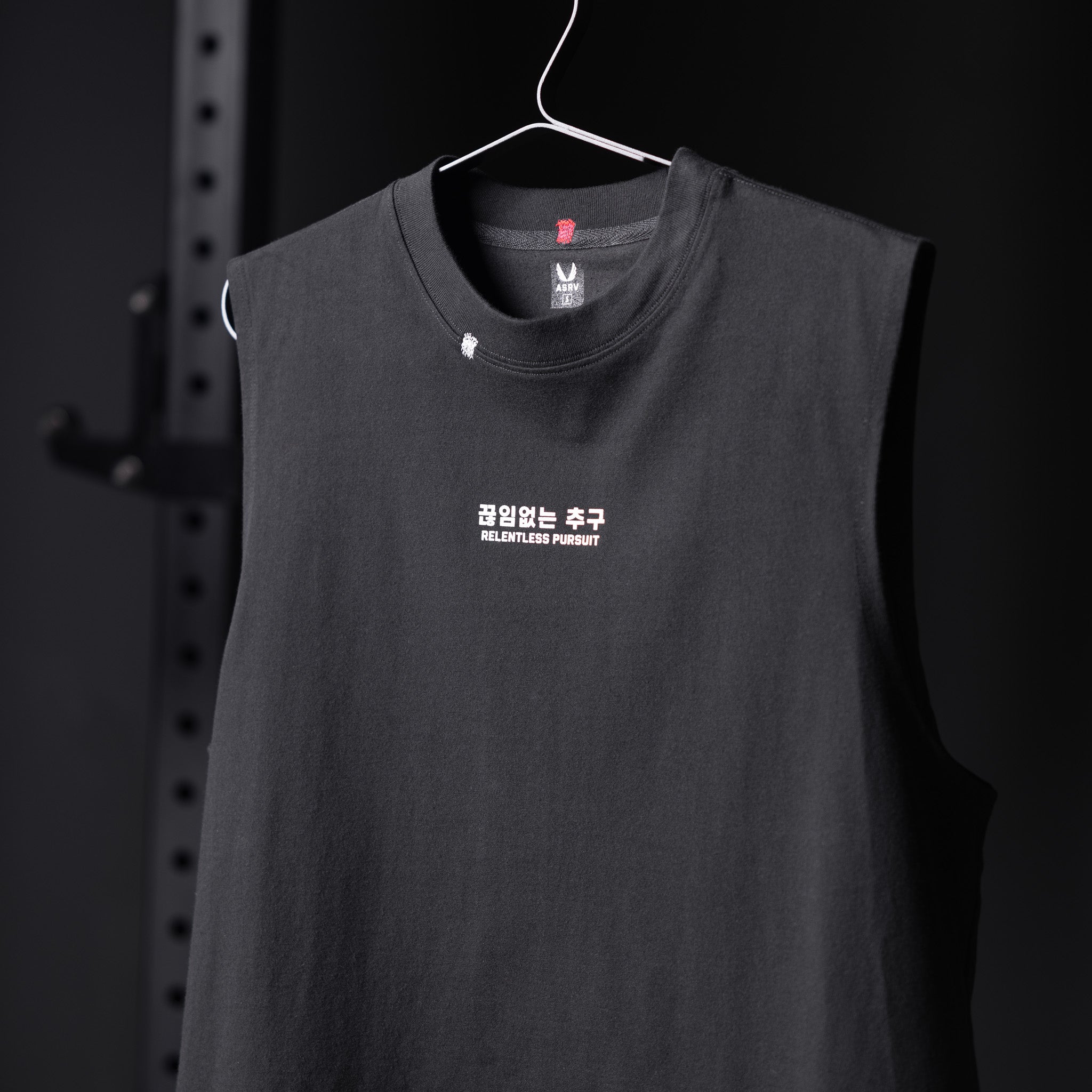 Black Tech Essential Relaxed Cutoff tank top on hanger with 'Relentless Pursuit' text design