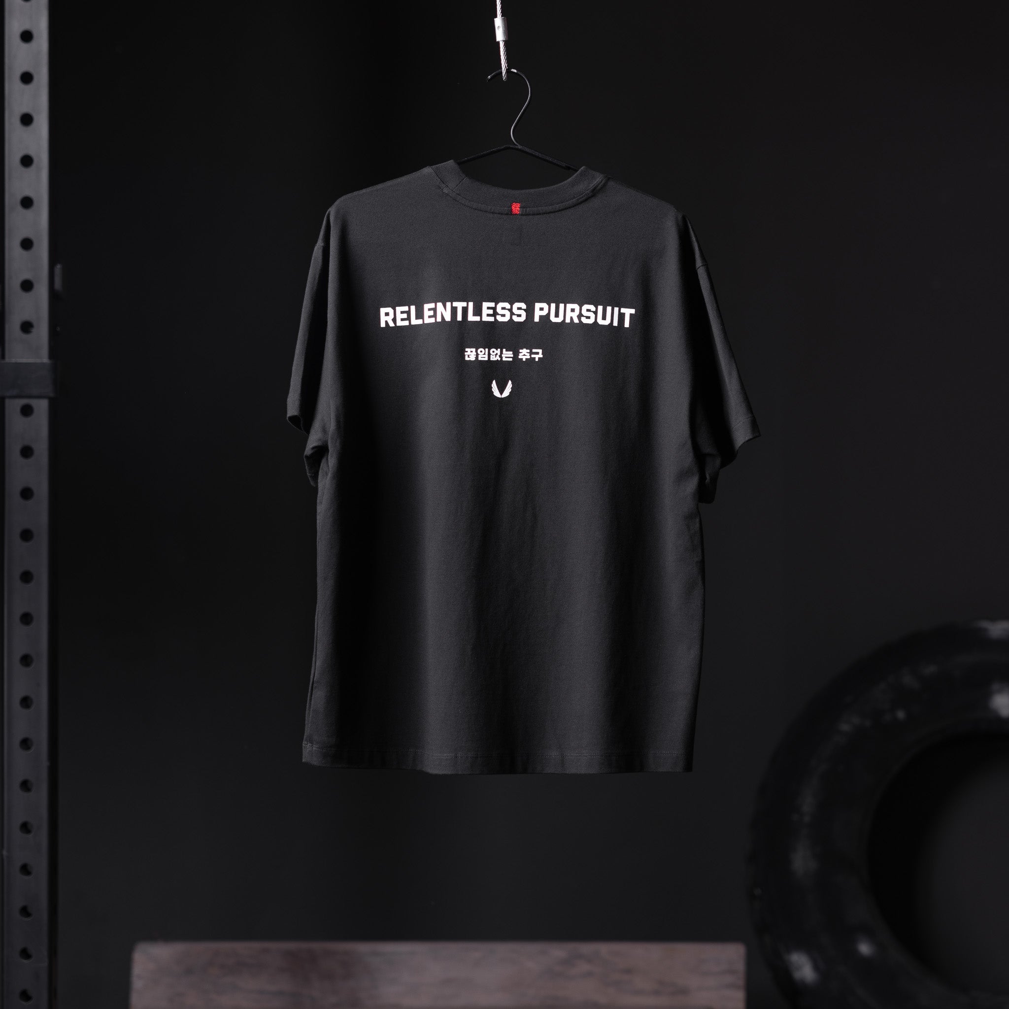 Black Tech Essential Relaxed Tee with 'Relentless Pursuit' graphic, hanging on hanger