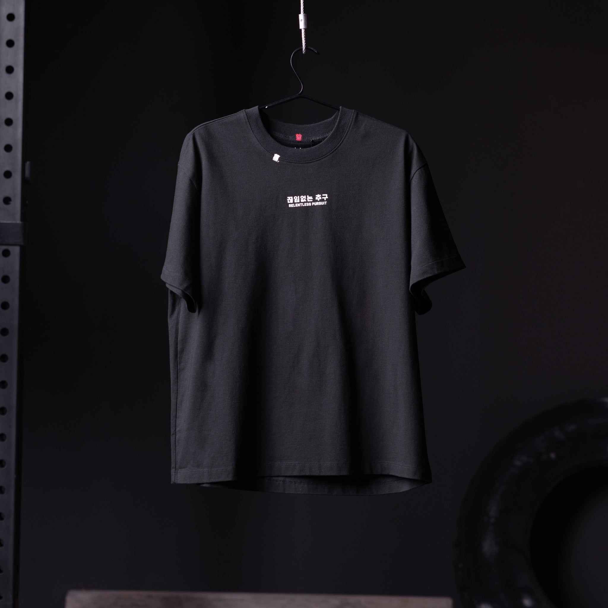 Black Tech Essential Relaxed Tee hanging on hanger against dark background