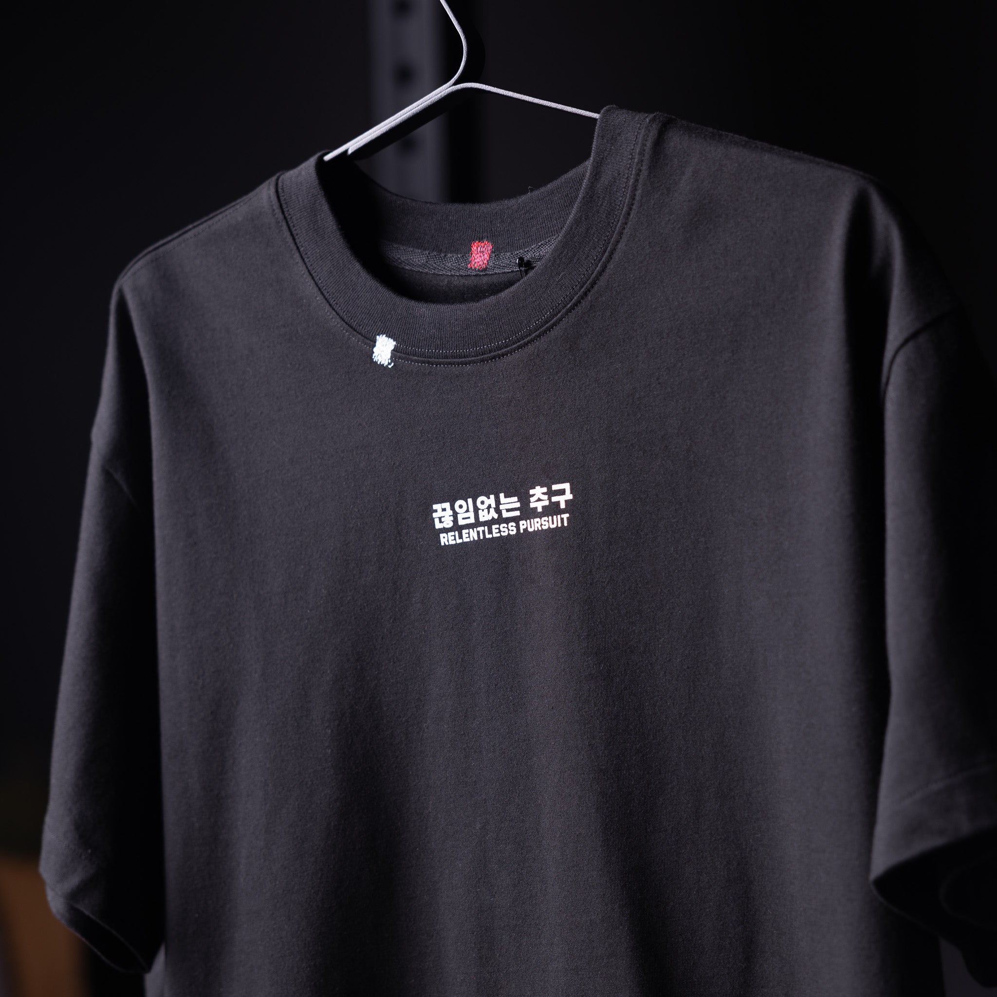 Black Tech Essential Relaxed Tee with 'Relentless Pursuit' text, displayed on hanger