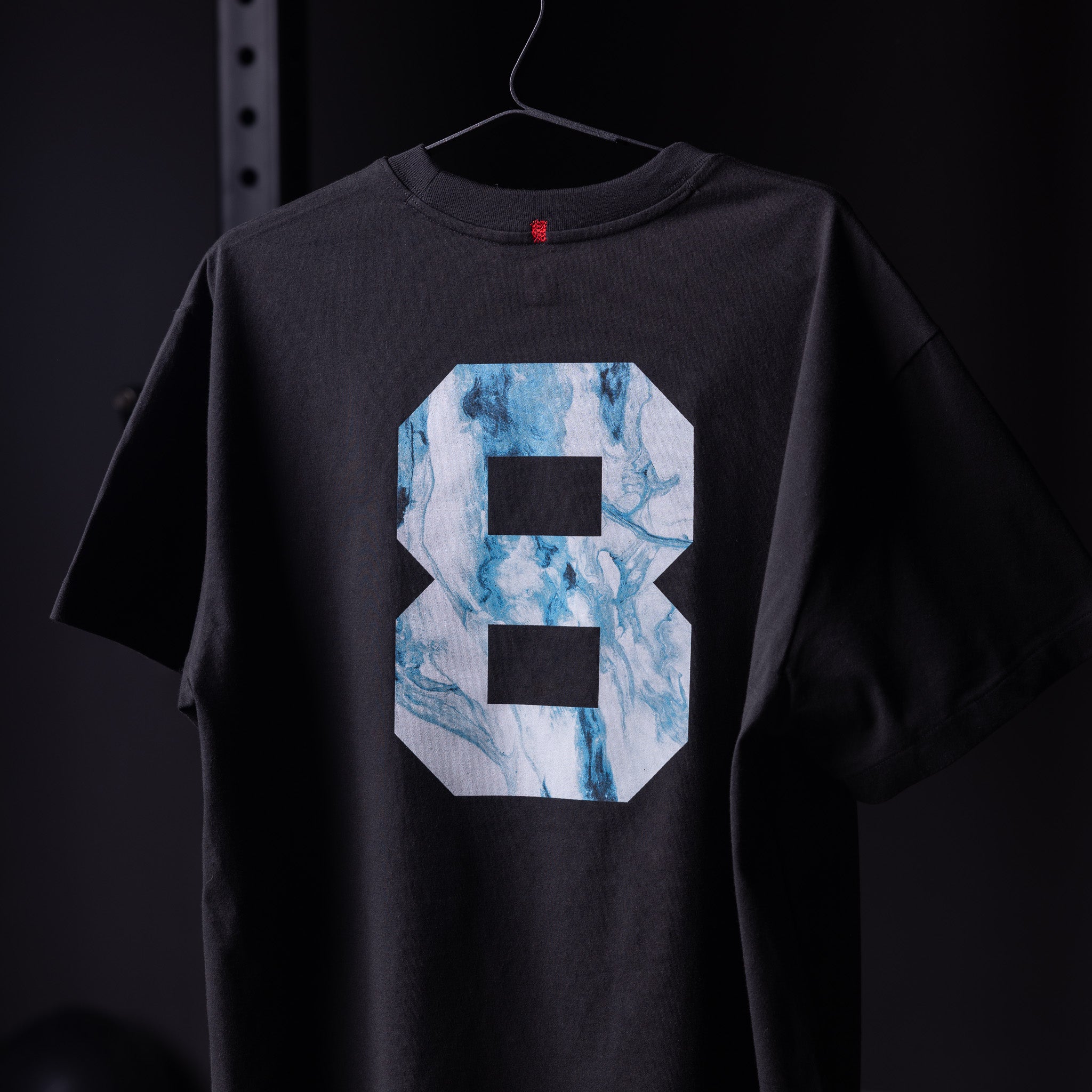 Black Tech Essential Relaxed Tee with blue marble number 8 graphic, back view on hanger
