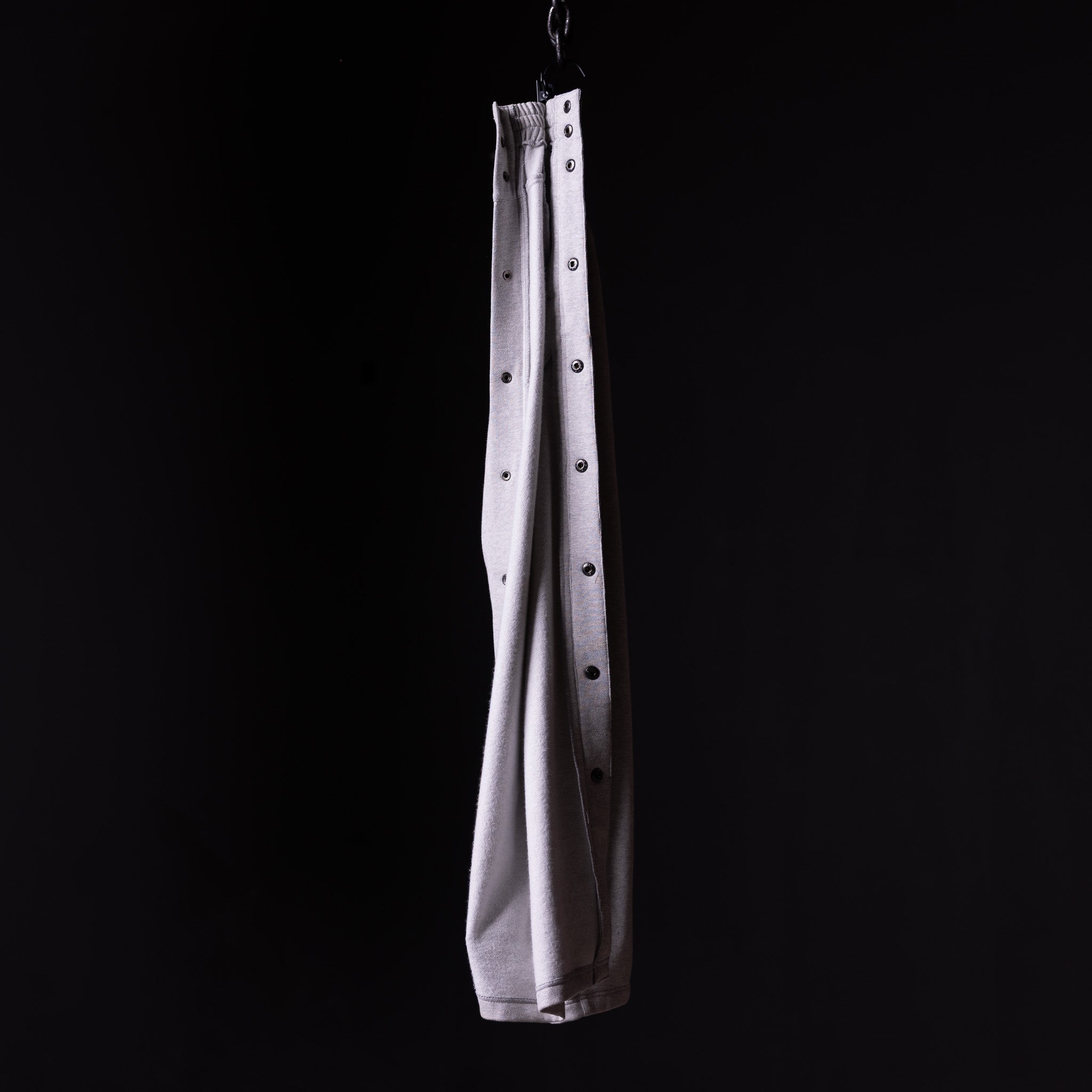 SP'22 Tearaway Jogger in light gray, hanging from hook against black background