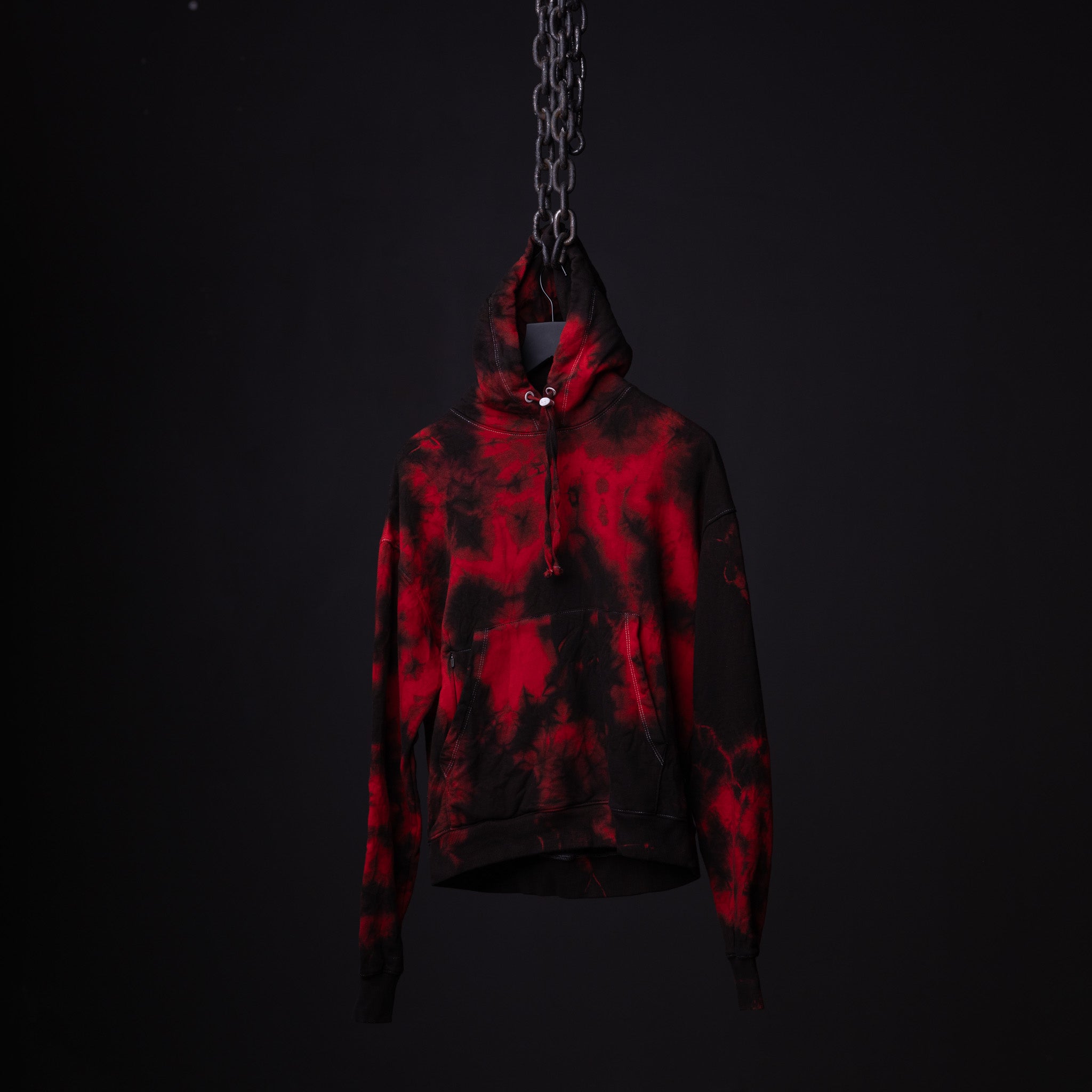 SM'22 Tie Dye Hoodie in red and black tie dye, suspended by chain against dark background