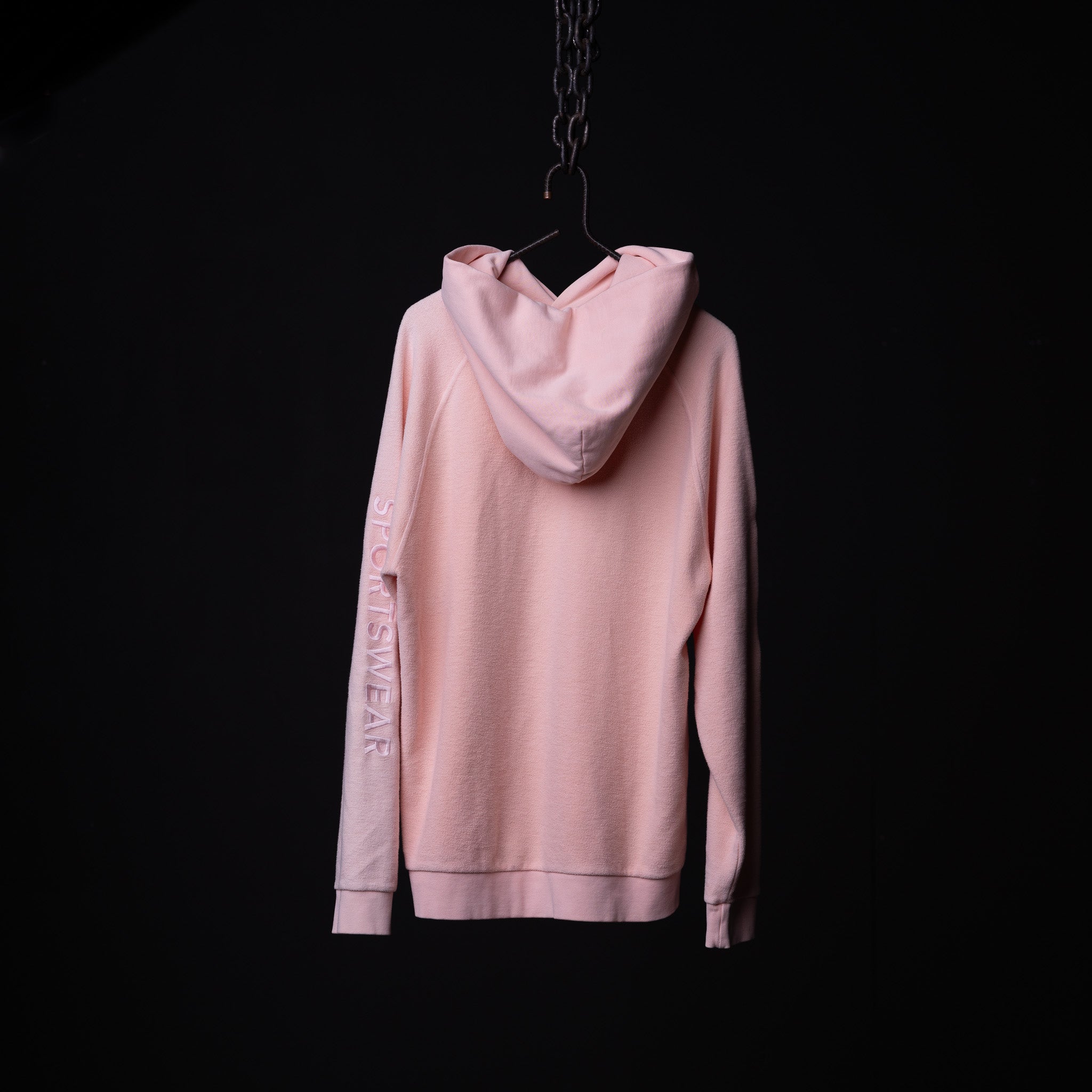 Pink reverse weave hoodie displayed on hanger, back view showing sleeve text