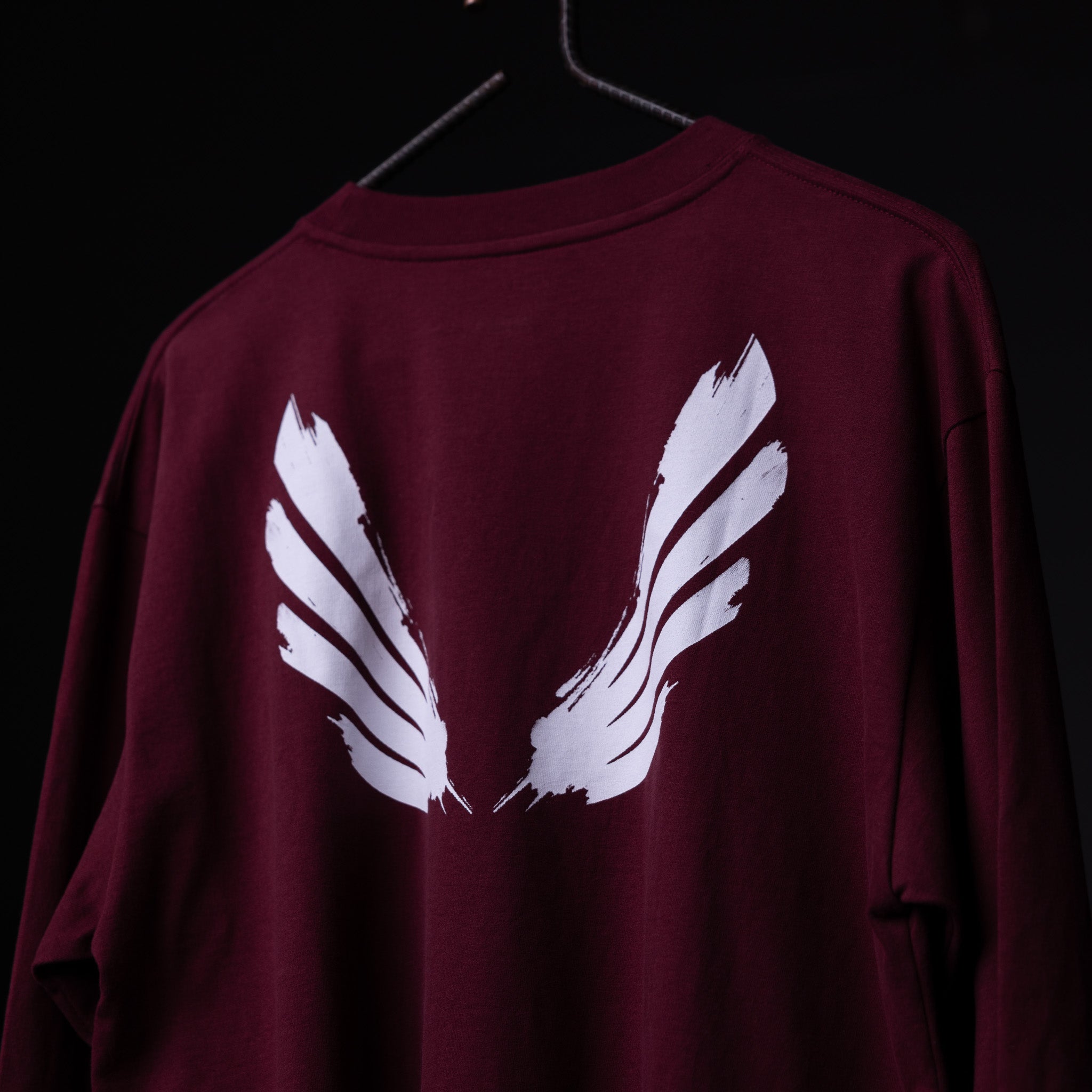 SM'22 Graphic Long Sleeve in maroon with white feather design, back view on hanger