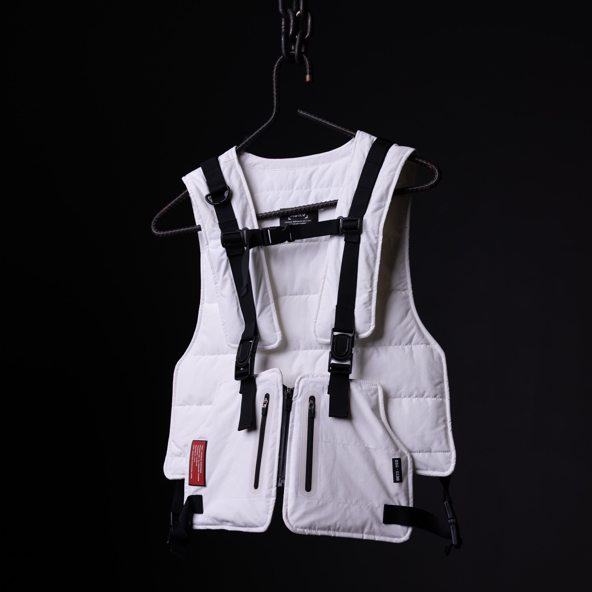 White technical vest with black straps and harness system displayed on hanger against black background
