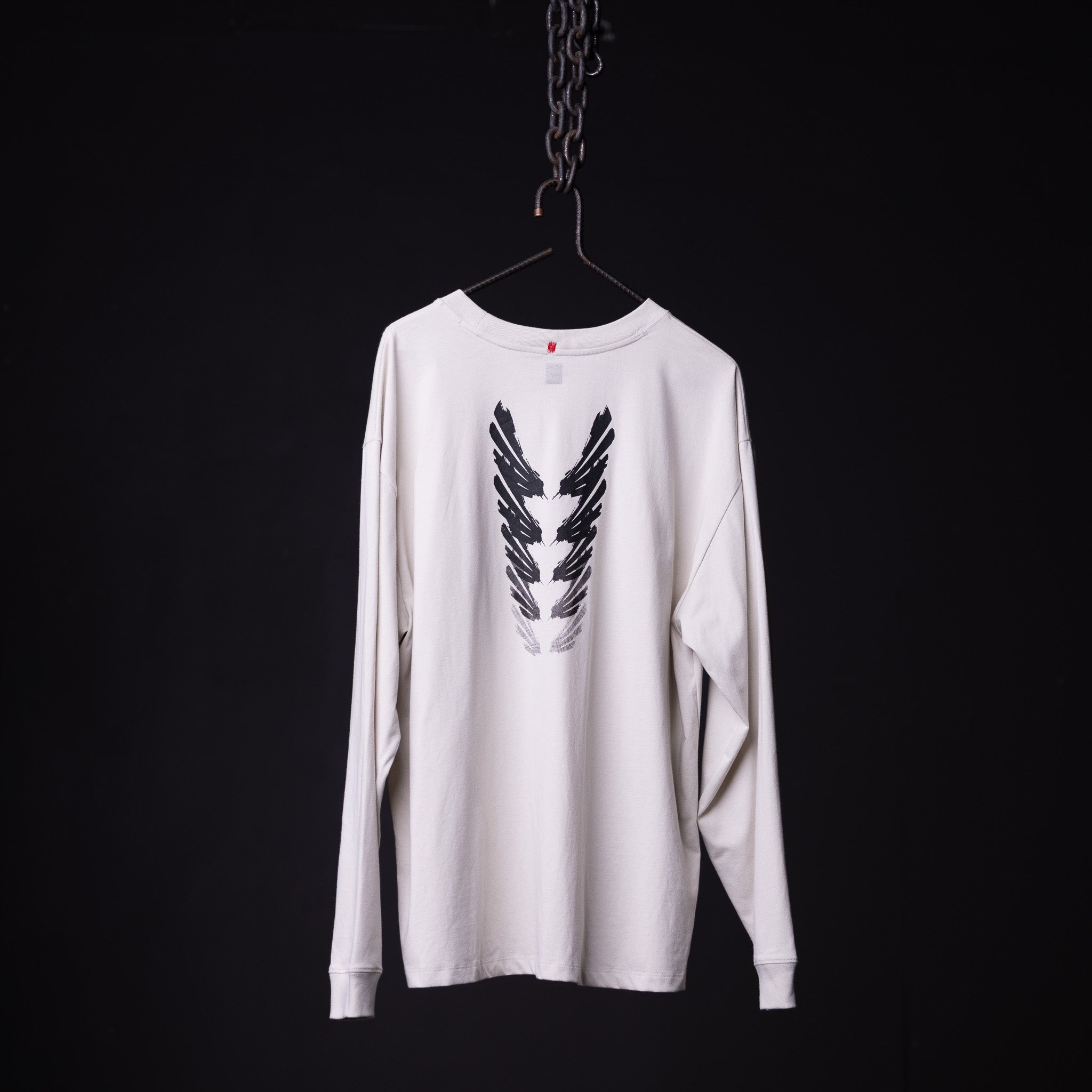 SP'23 Graphic Long Sleeve white long-sleeve tee with black feather wing design, hung on hanger