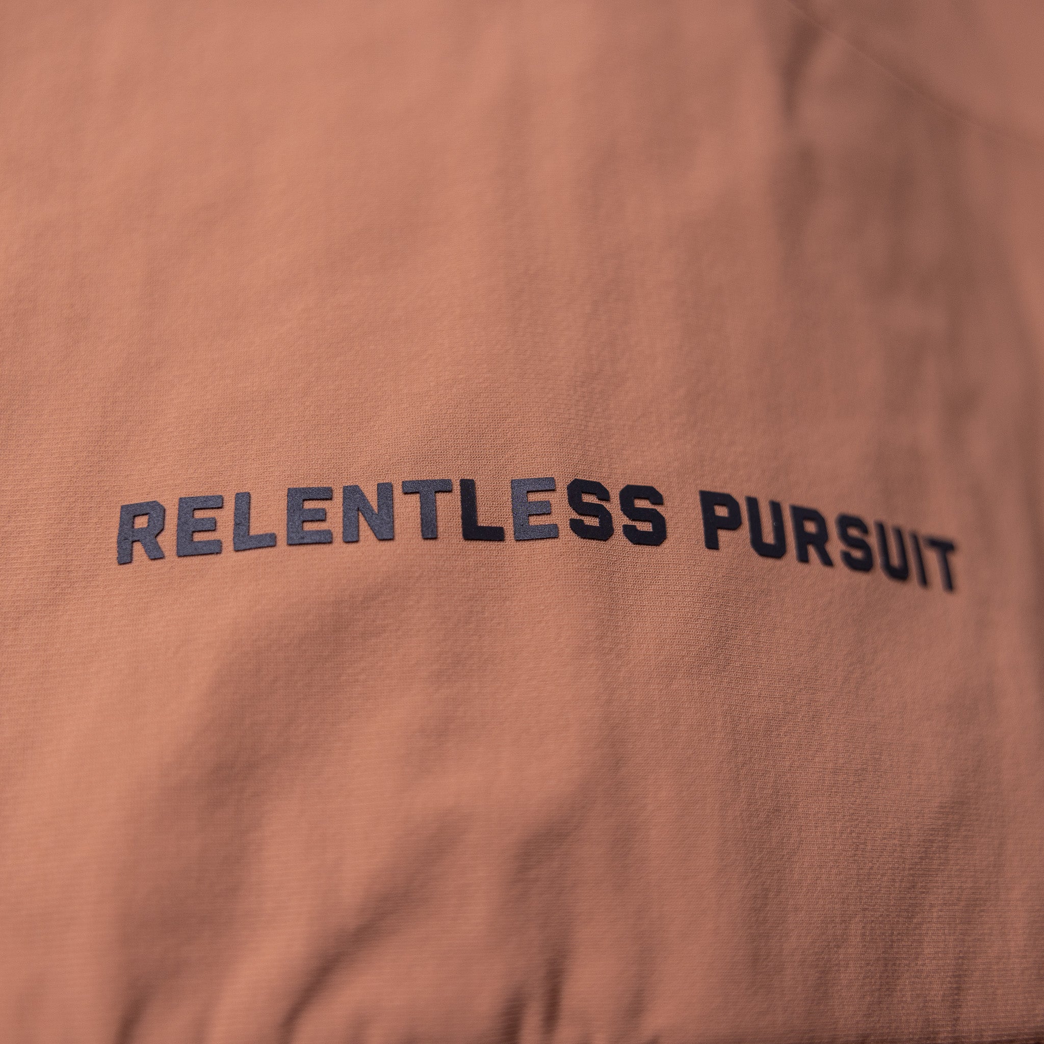FA'22 Insulated Gilet Vest in rust, close-up detail of 'Relentless Pursuit' text on fabric
