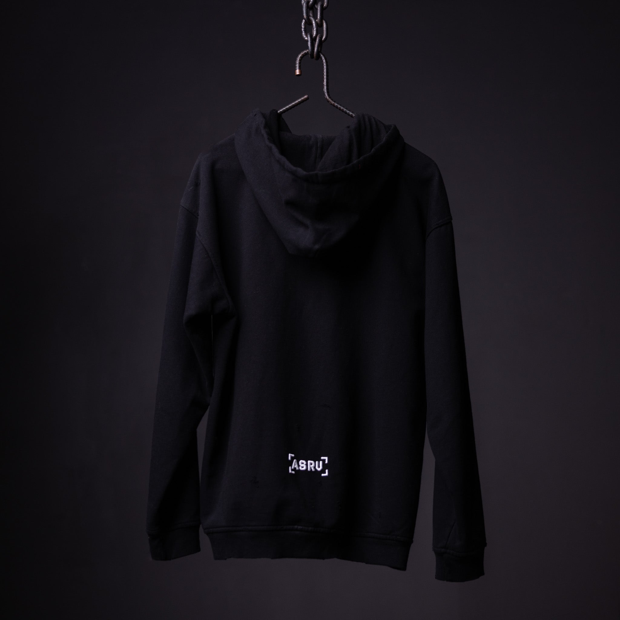 Black distressed hoodie on hanger against dark background, back view showing logo