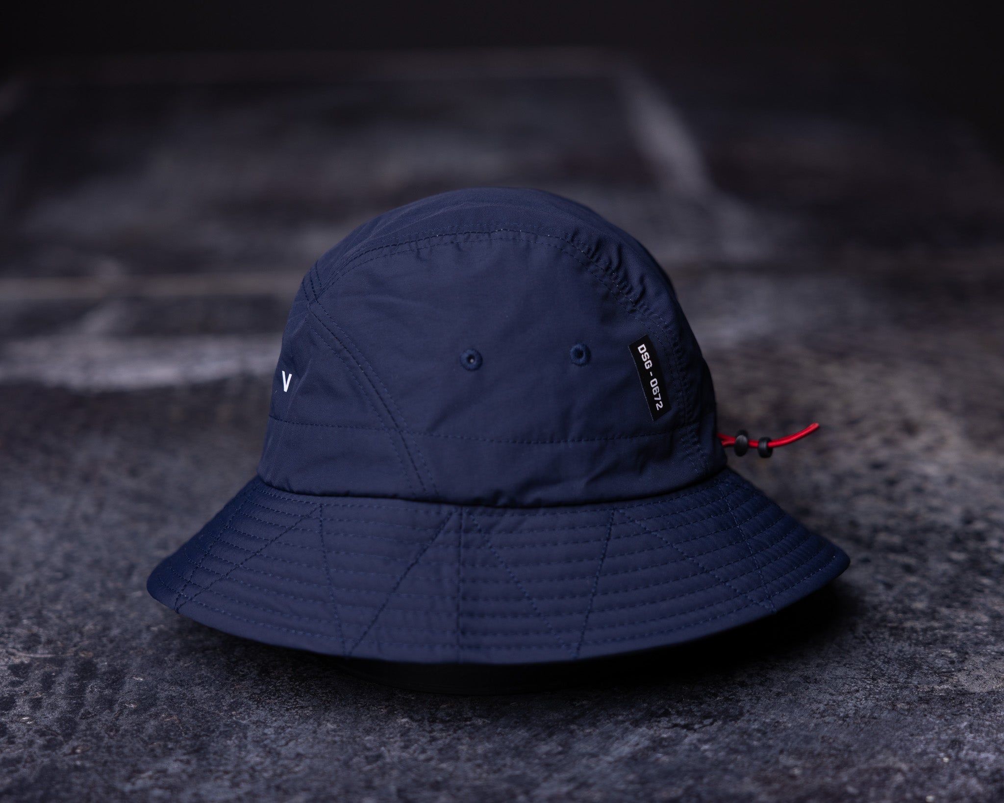 flatlay WN'22 Cinch Bucket Hat in navy blue, overhead view on dark surface