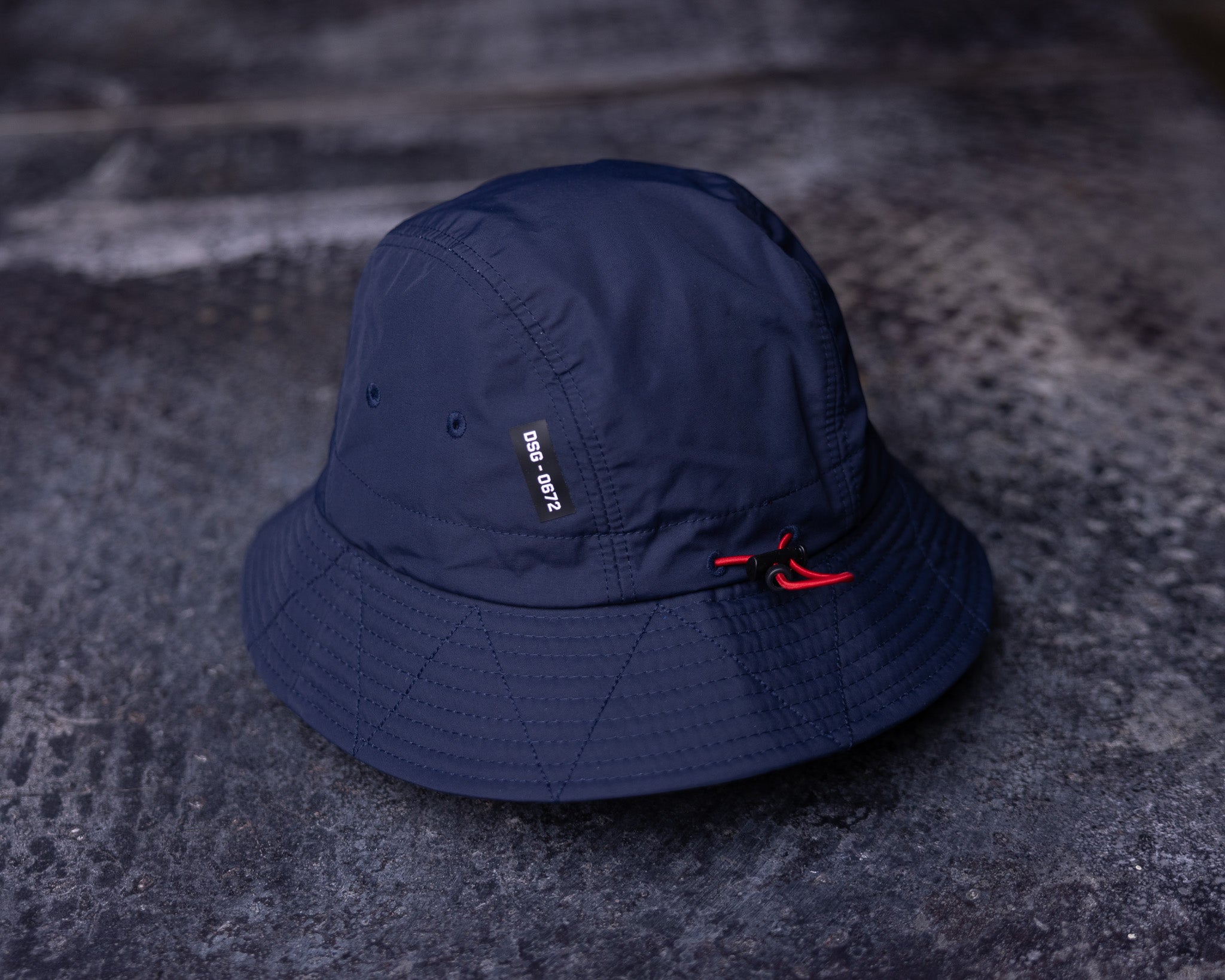 flatlay WN'22 Cinch Bucket Hat in navy blue, top view on textured surface