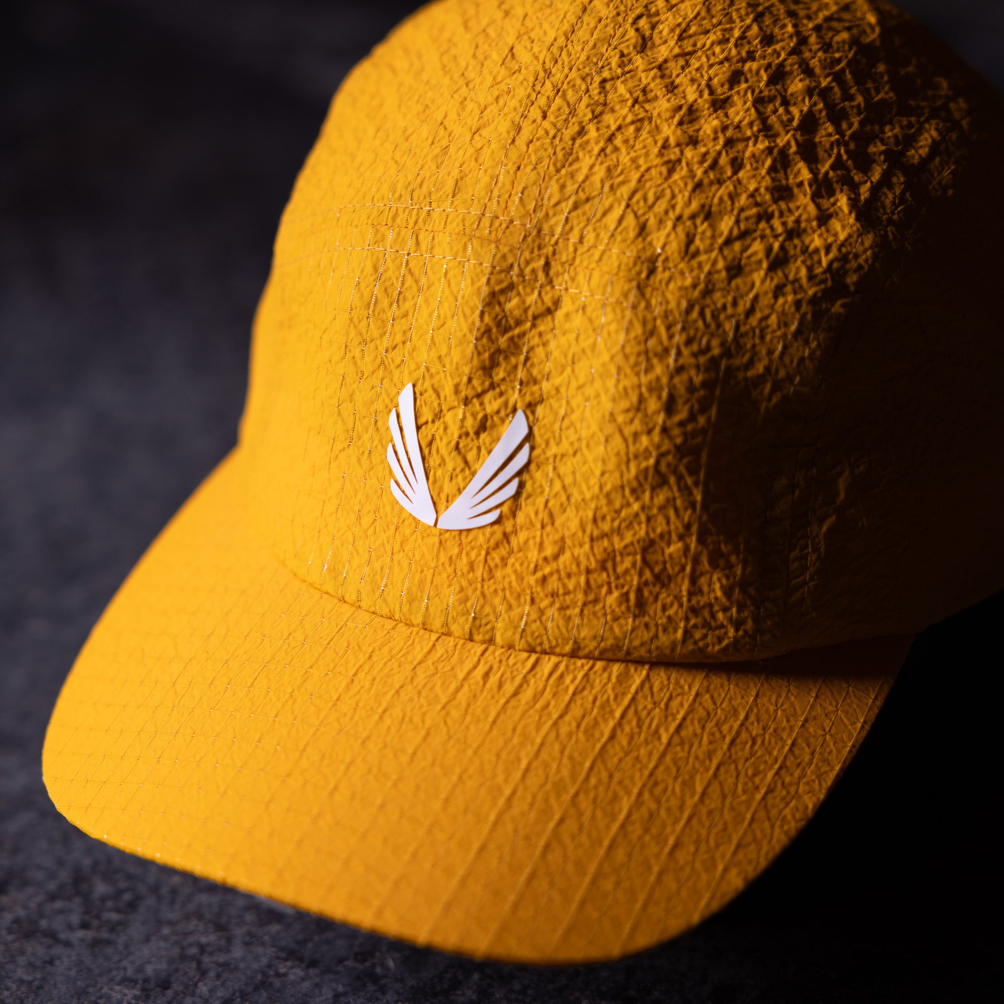 flatlay WN'23 5 Panel Hat in golden yellow, front view on dark surface