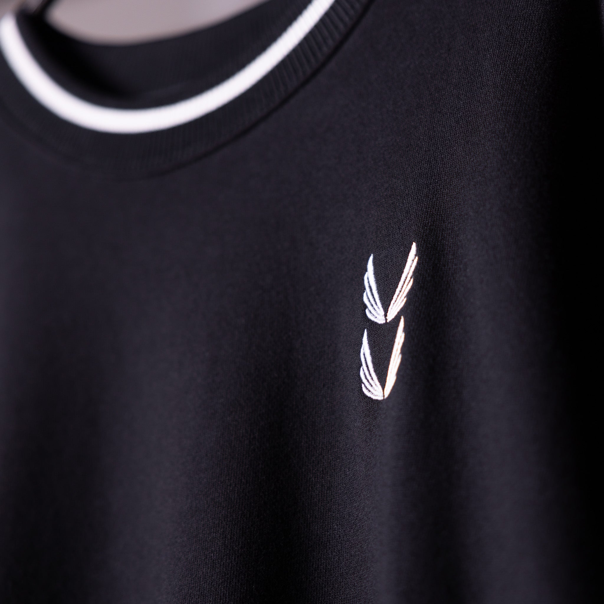 Black crew neck sweatshirt with white winged logo detail, worn on model