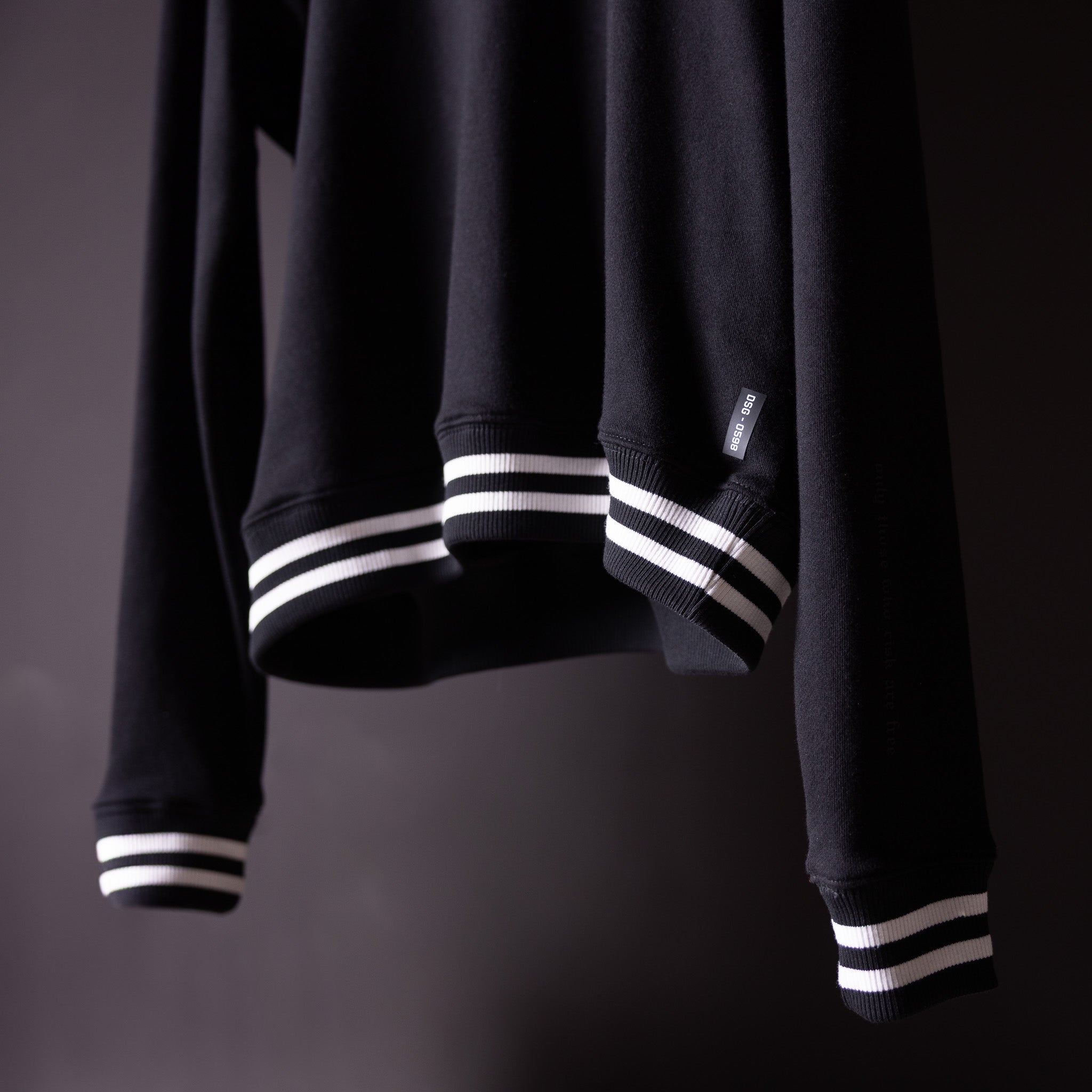 Black crew neck sweatshirt with white striped ribbed cuffs, detail view of sleeves