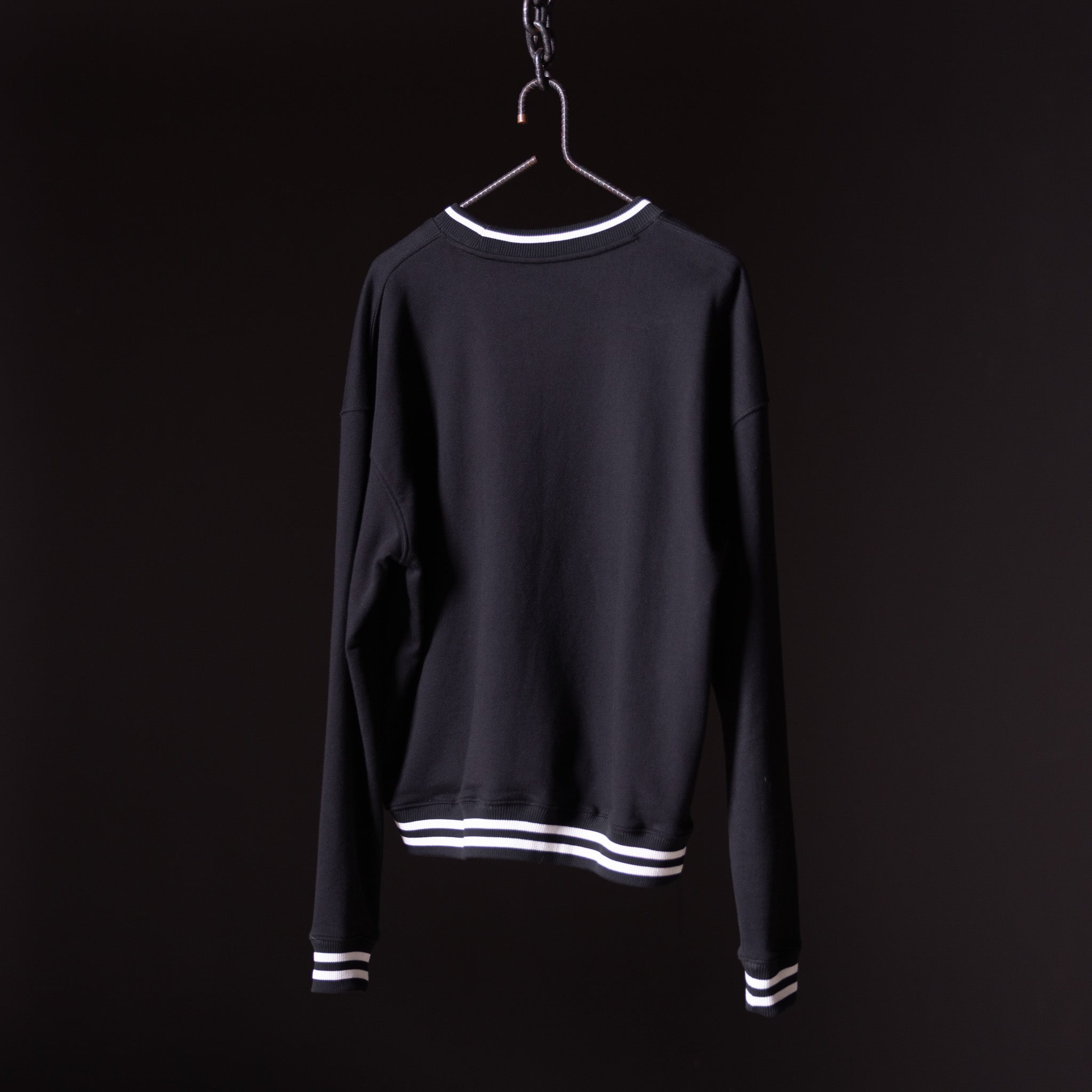 Black crew neck sweatshirt with white stripe trim, displayed on hanger against dark background