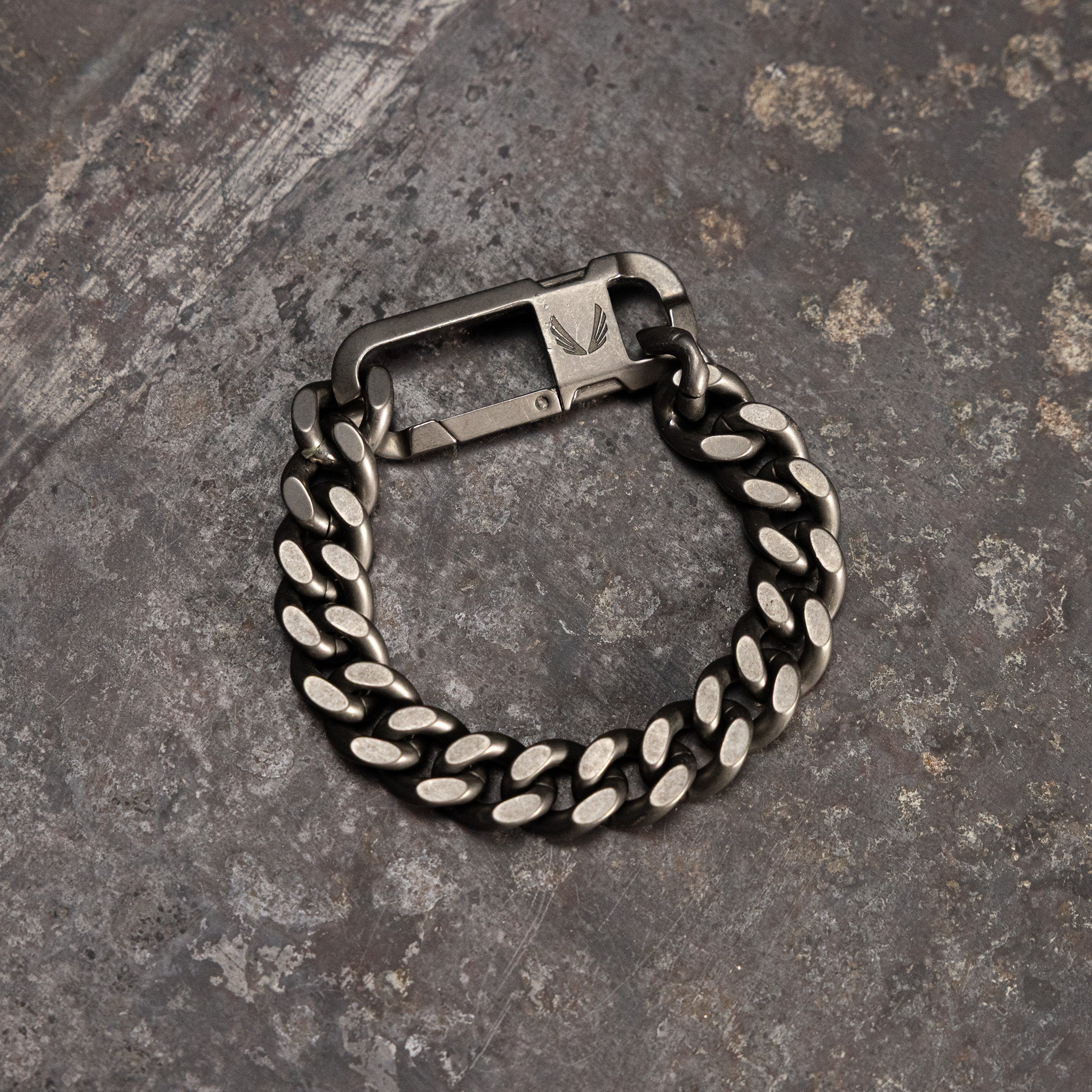 Carabiner Curb Bracelet in silver-tone metal, overhead view on textured grey surface