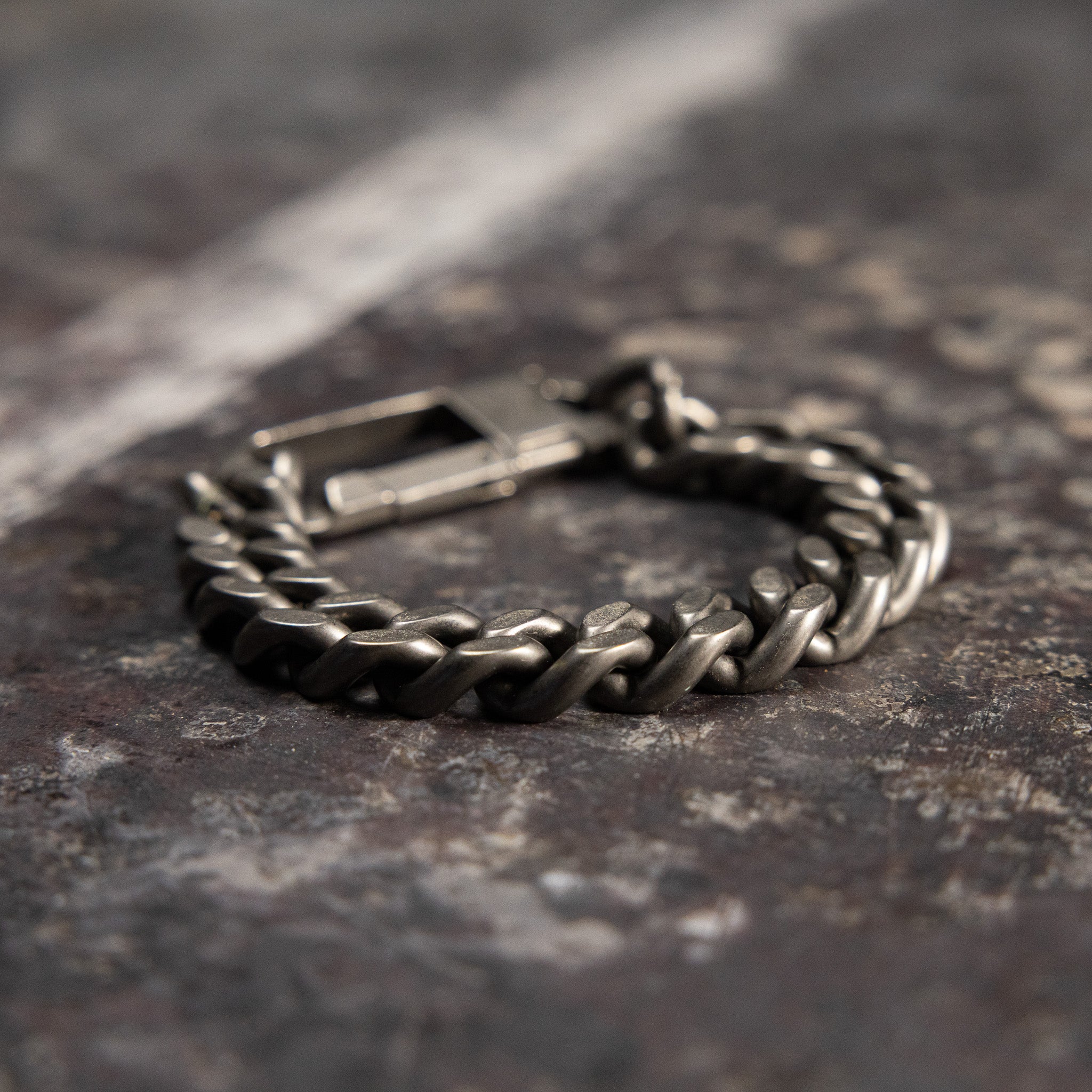 Flatlay of Carabiner Curb Bracelet in silver, overhead view on textured gray surface