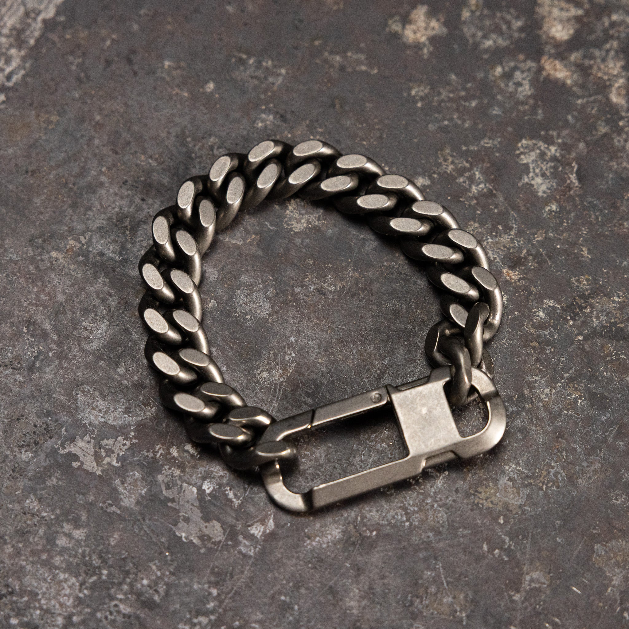 Carabiner Curb Bracelet in silver, top view on textured gray surface