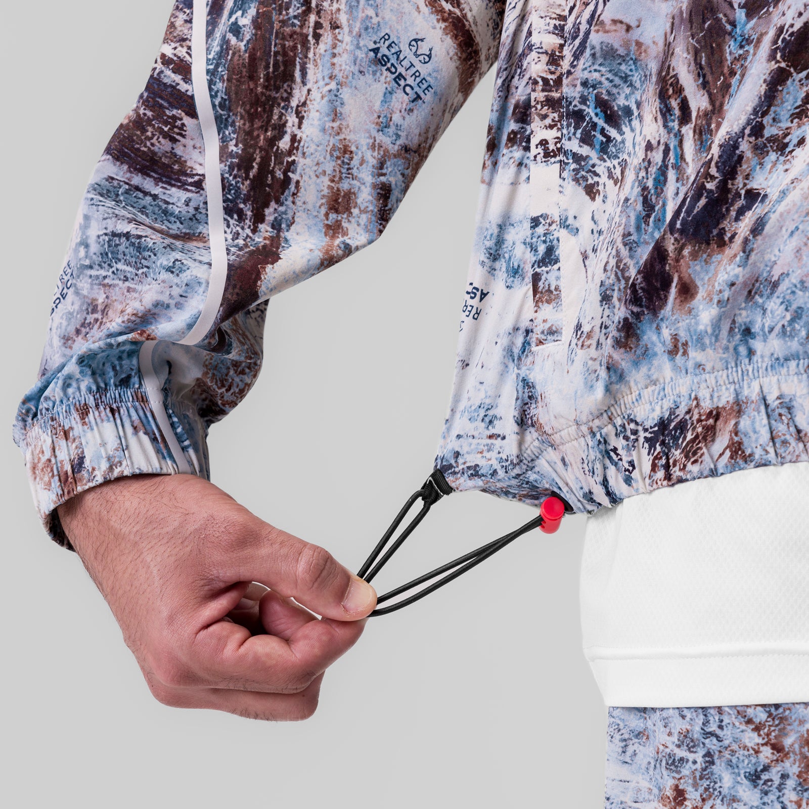 Aerotex Track Jacket in blue/brown camo, model wearing jacket with hand detail showing drawcord