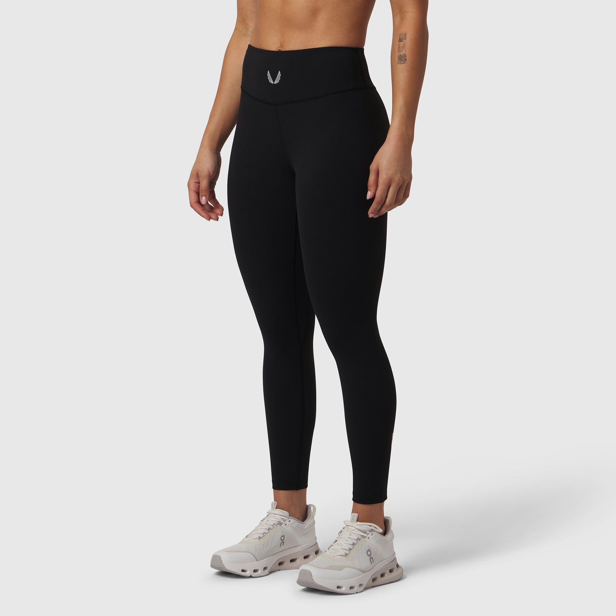 Black LYCRA® ADAPTIV legging worn by model, full-length side view with white sneakers