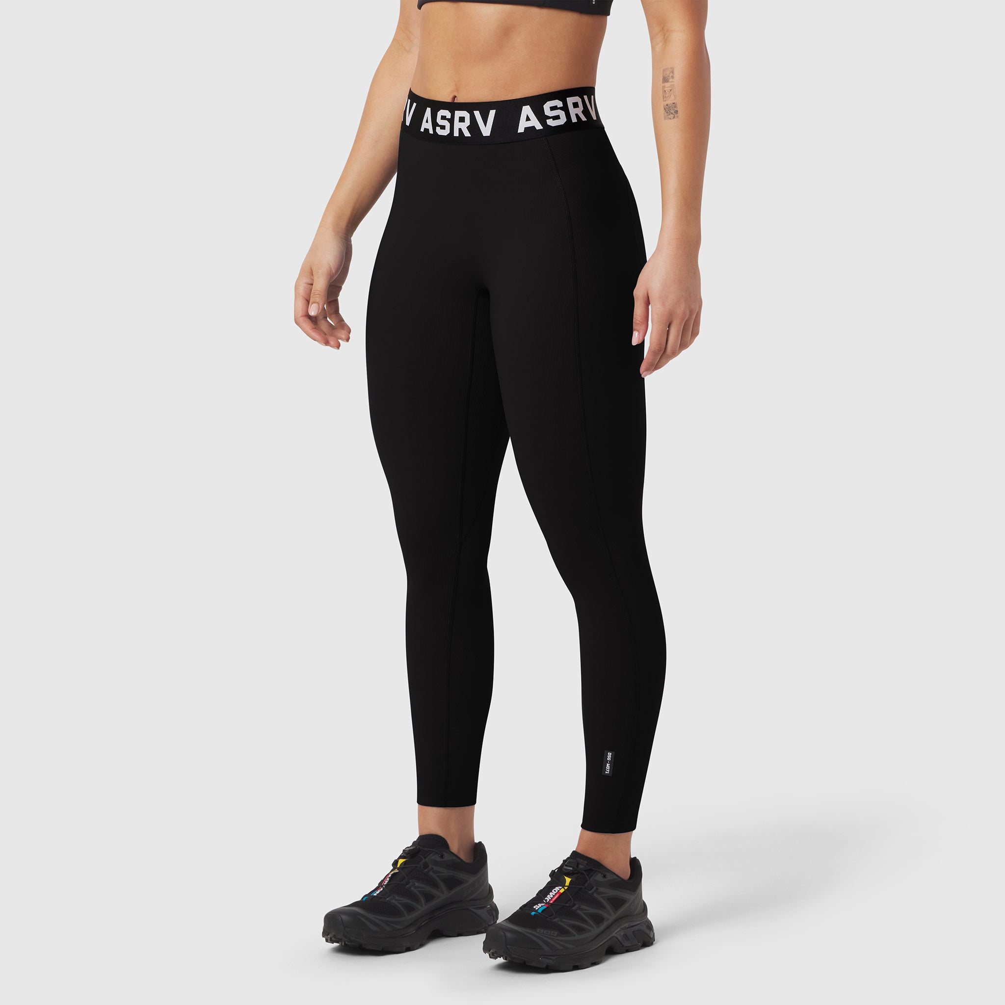 Black LYCRA® ribbed leggings worn by model with black sneakers, front view
