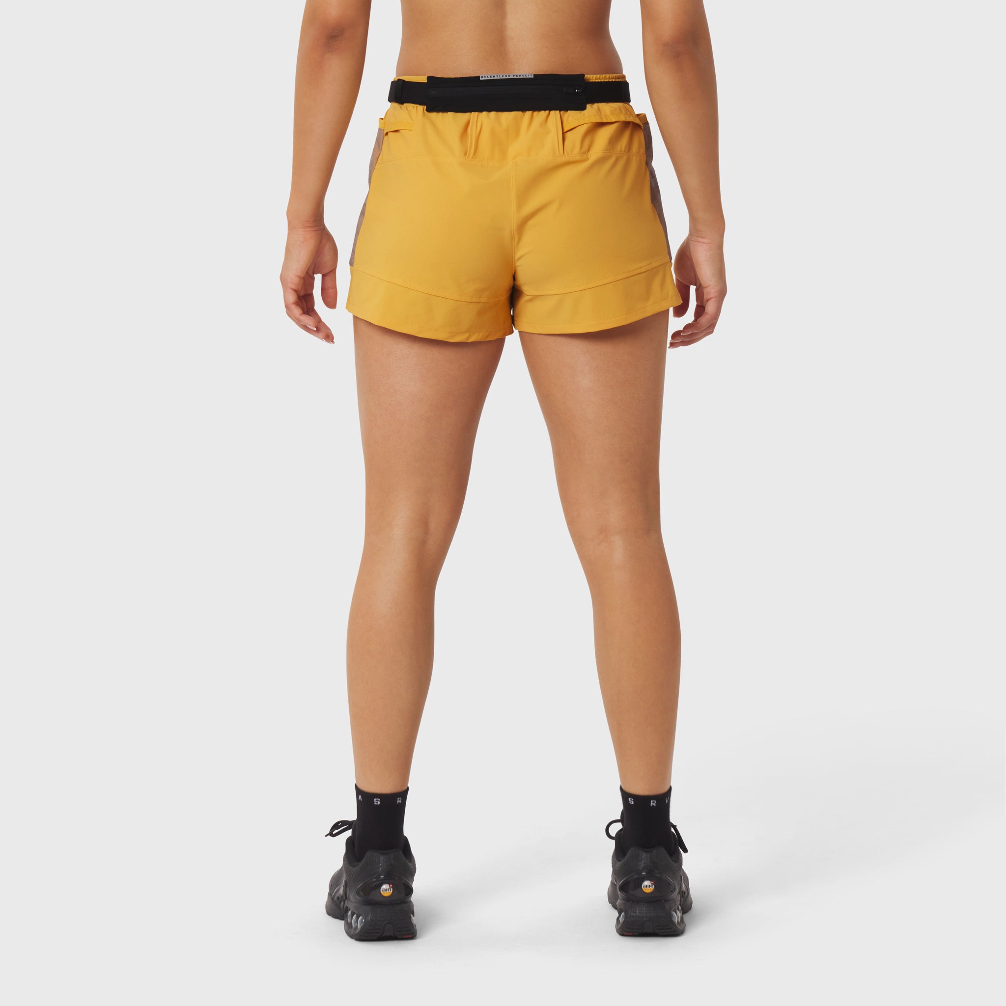 Woman wearing yellow athletic shorts with black waistband, rear view, standing with hands at sides