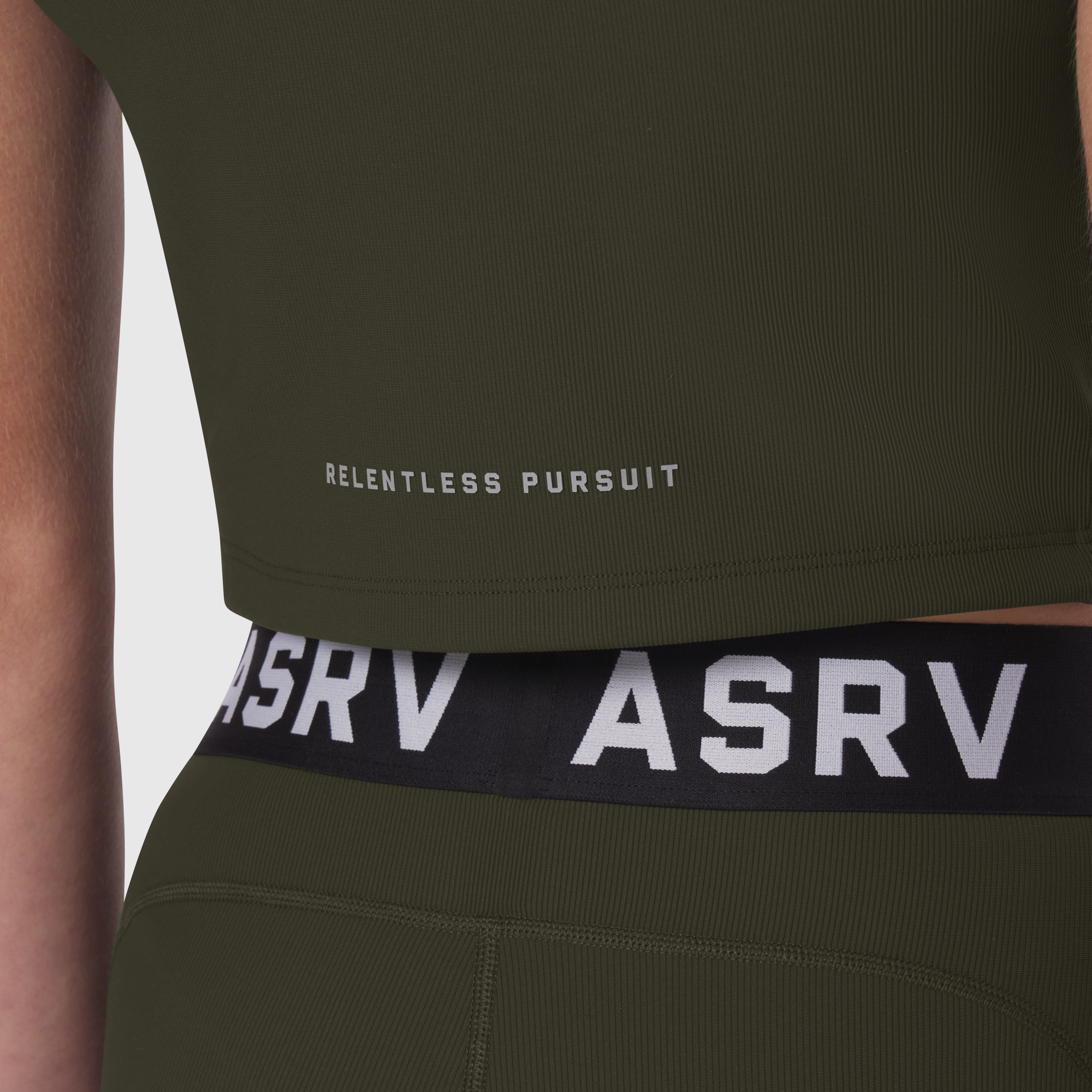 Lycra ribbed mockneck tank in olive worn by model, showing 'RELENTLESS PURSUIT' text and ASRV waistband detail