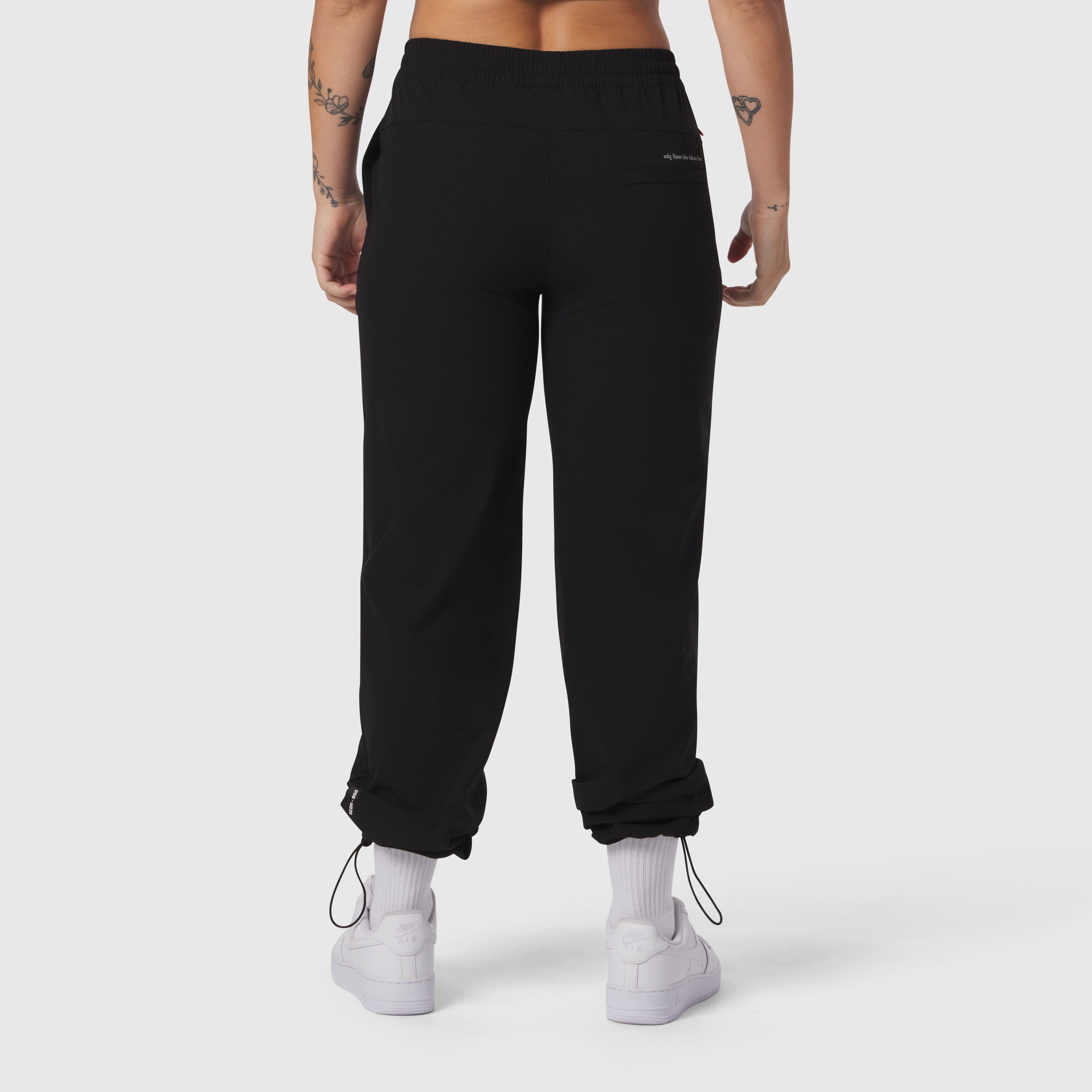 Black ripstop relaxed track pant worn by model, back view with cuffed ankles and white sneakers