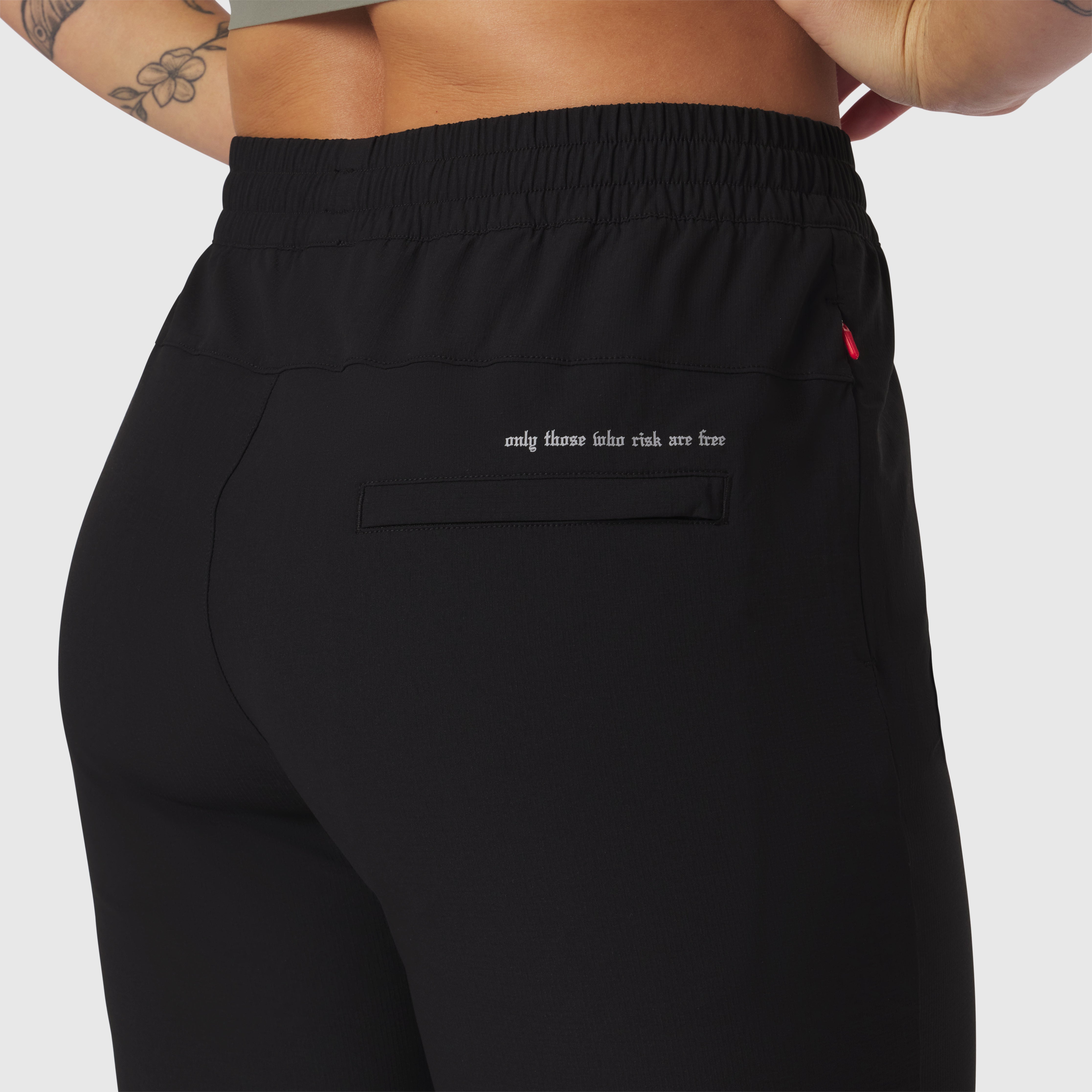 Black ripstop relaxed track pant worn by model, back view showing pocket detail and text