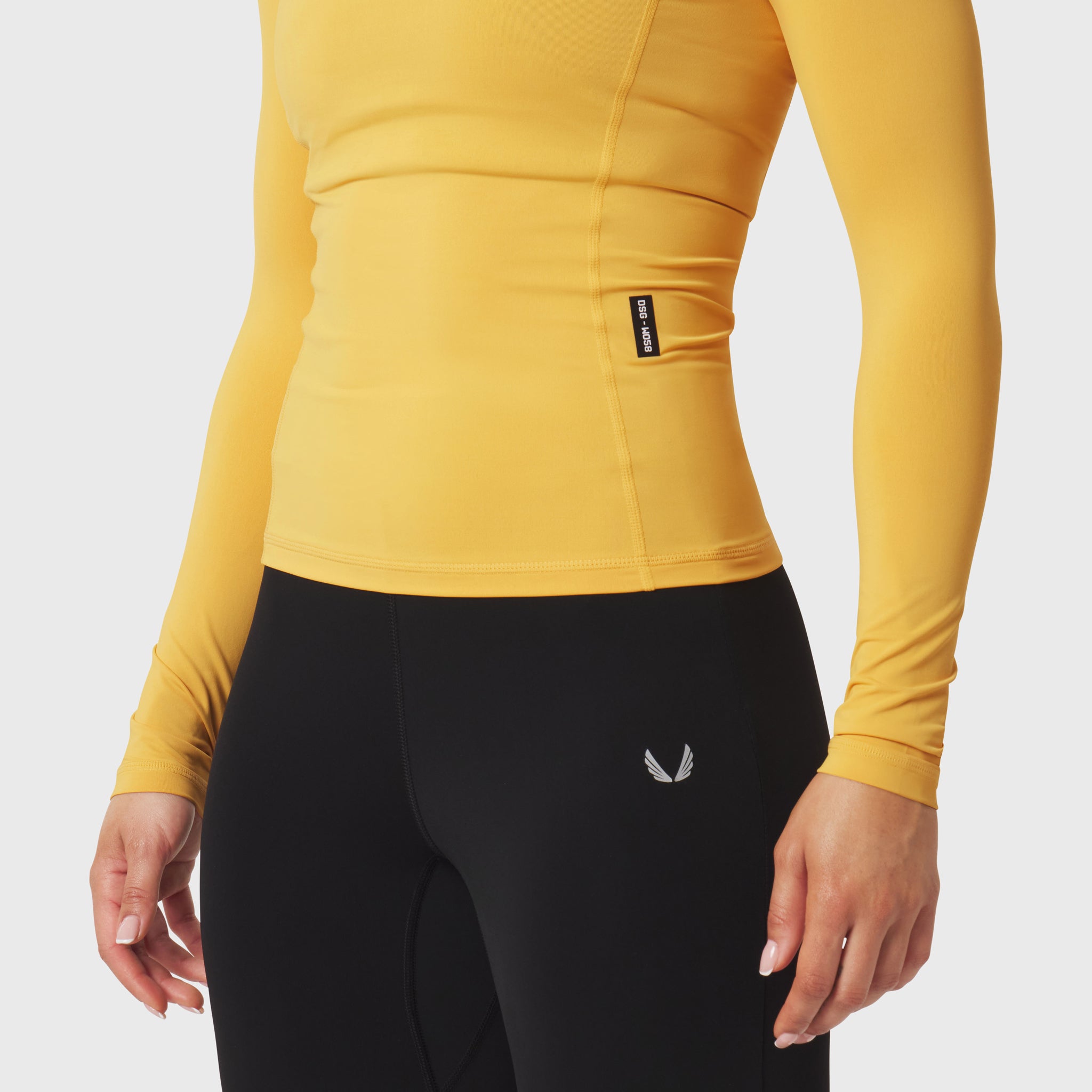 LYCRA® ADAPTIV Baselayer Longsleeve in amber yellow, worn with black leggings, side view