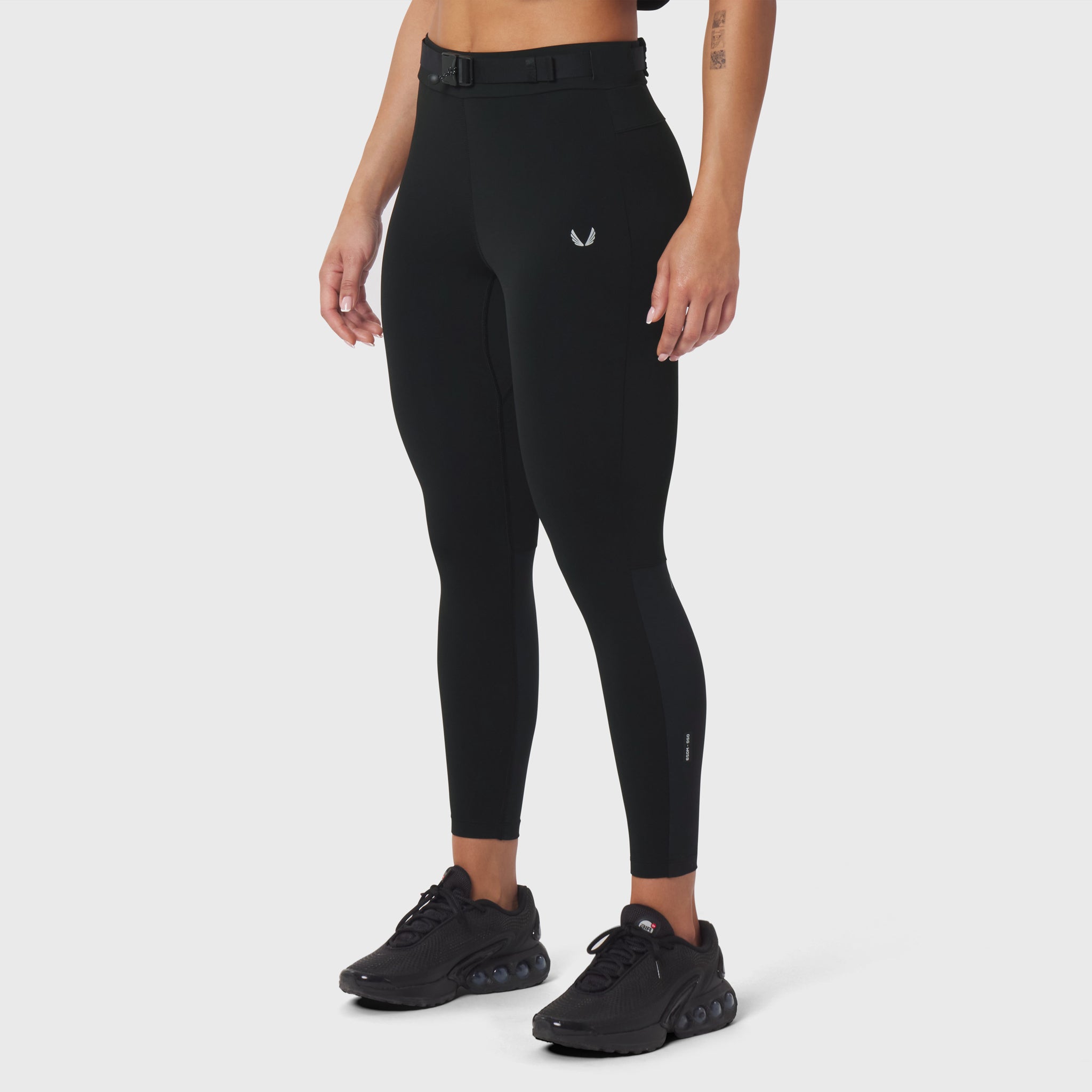 W059 Hybrid Belt-Pack Run Legging in black, worn by model with black sneakers, side view