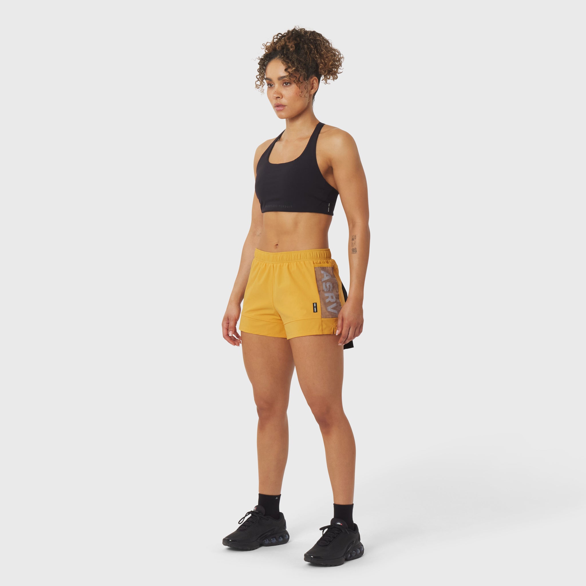 Tetra-Lite® Adventure Short in amber, worn by model with black sports bra, full-body side view