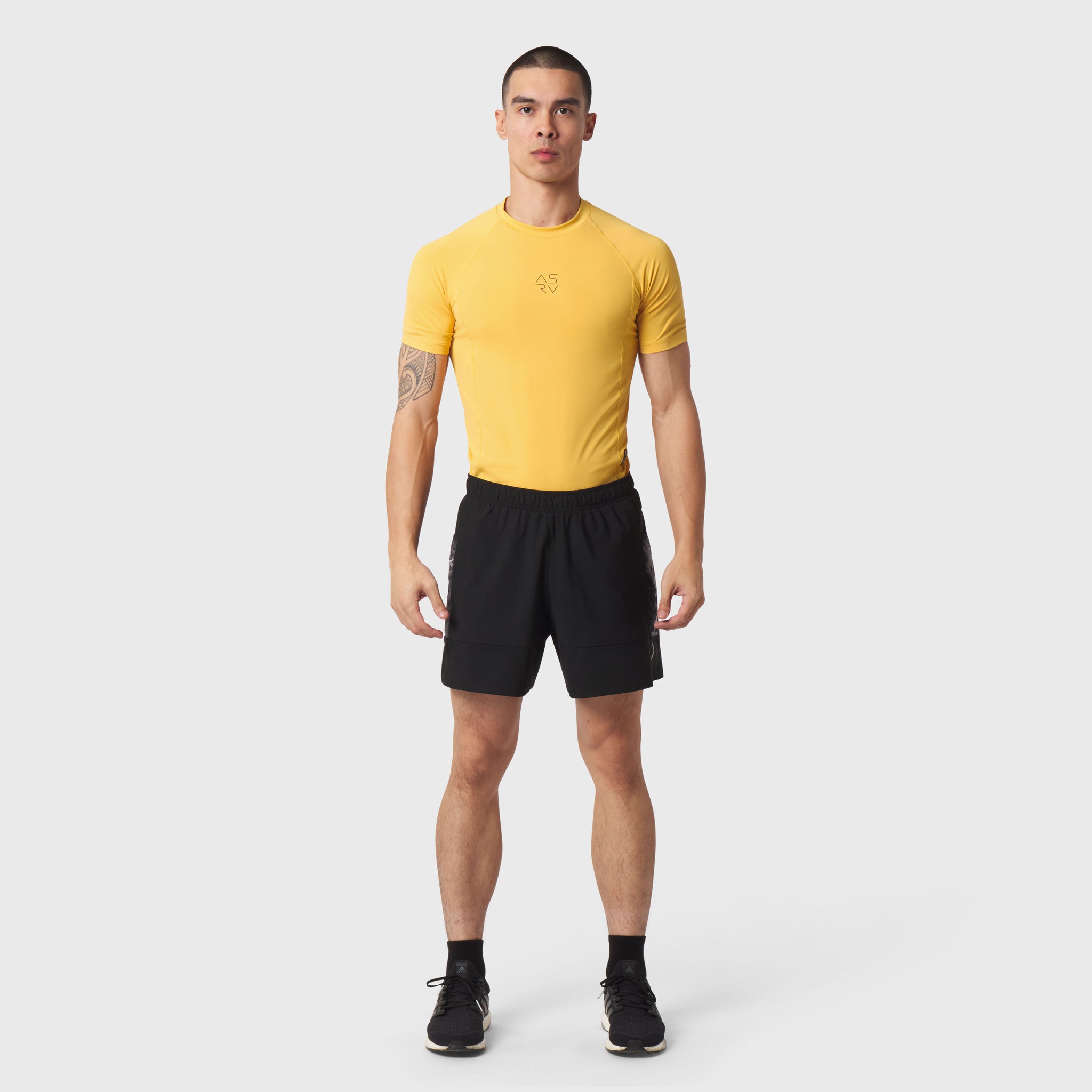 LYCRA® ADAPTIV Baselayer Shortsleeve in amber yellow worn with black shorts, front view