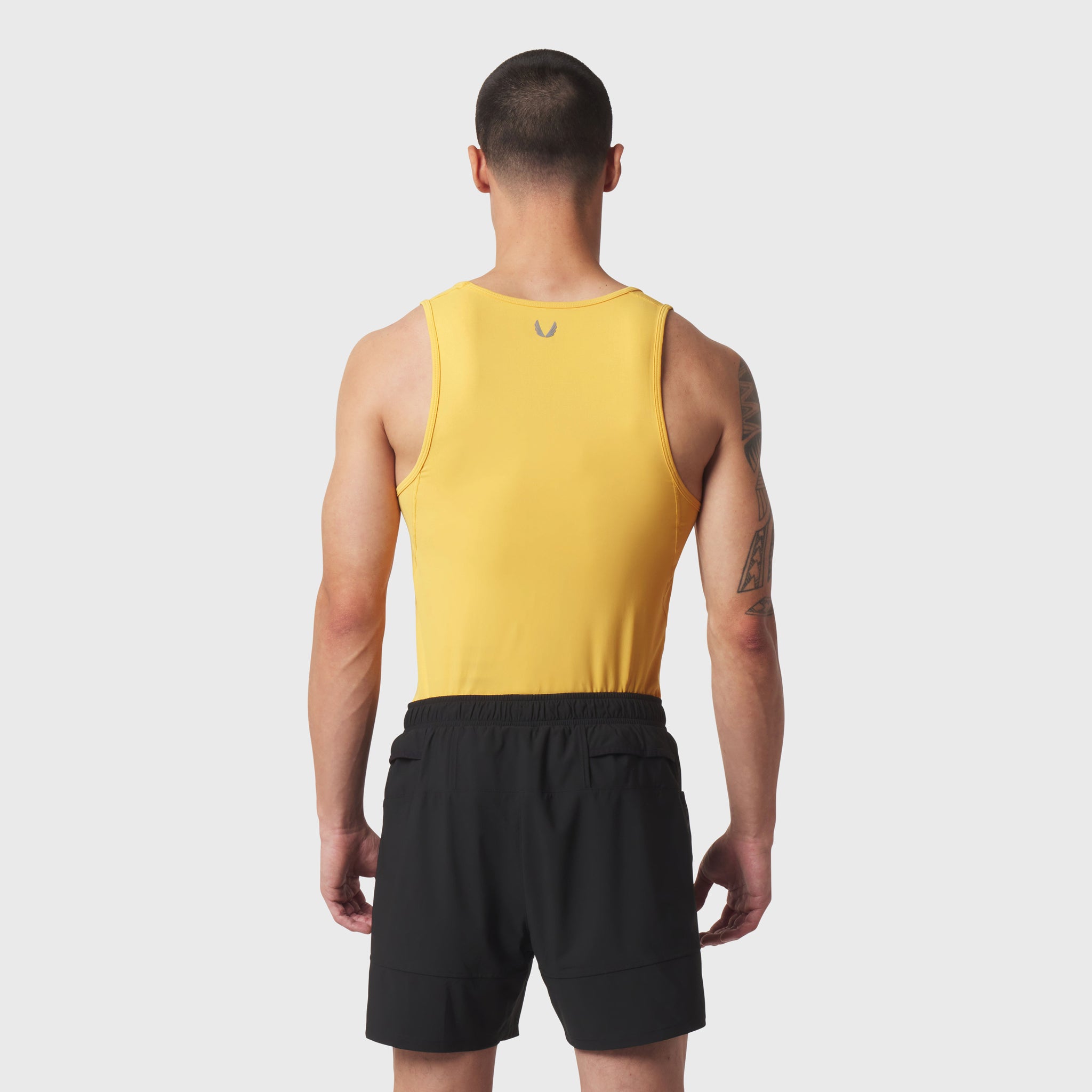 Amber LYCRA® ADAPTIV baselayer tank on model, back view, paired with black shorts