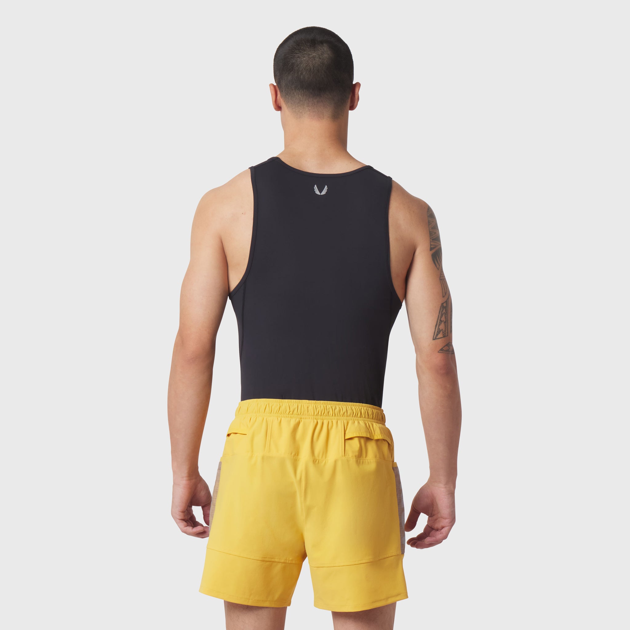 Black LYCRA® ADAPTIV baselayer tank on model, rear view, paired with yellow shorts
