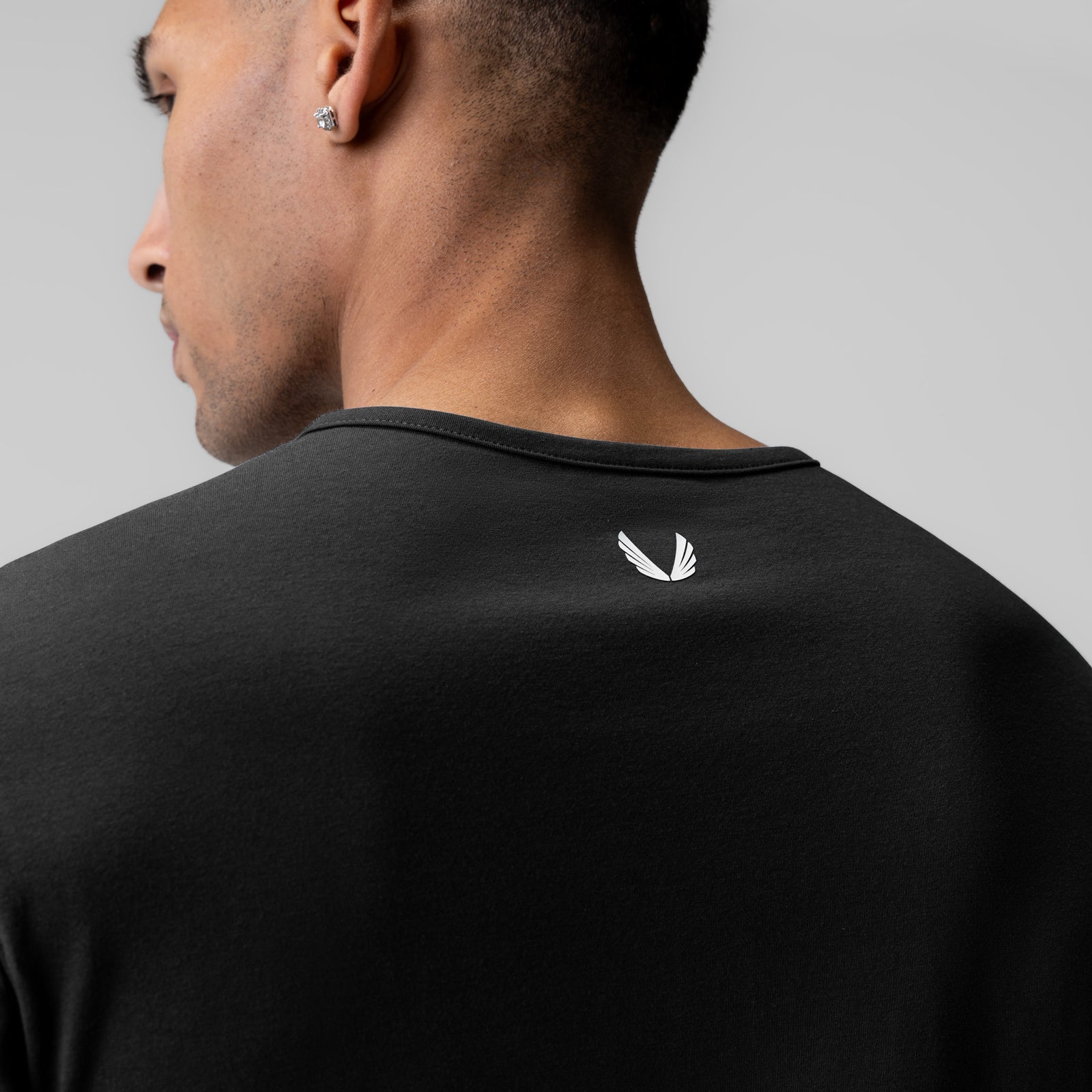 Black long sleeve shirt worn by model, rear view showing white feather logo