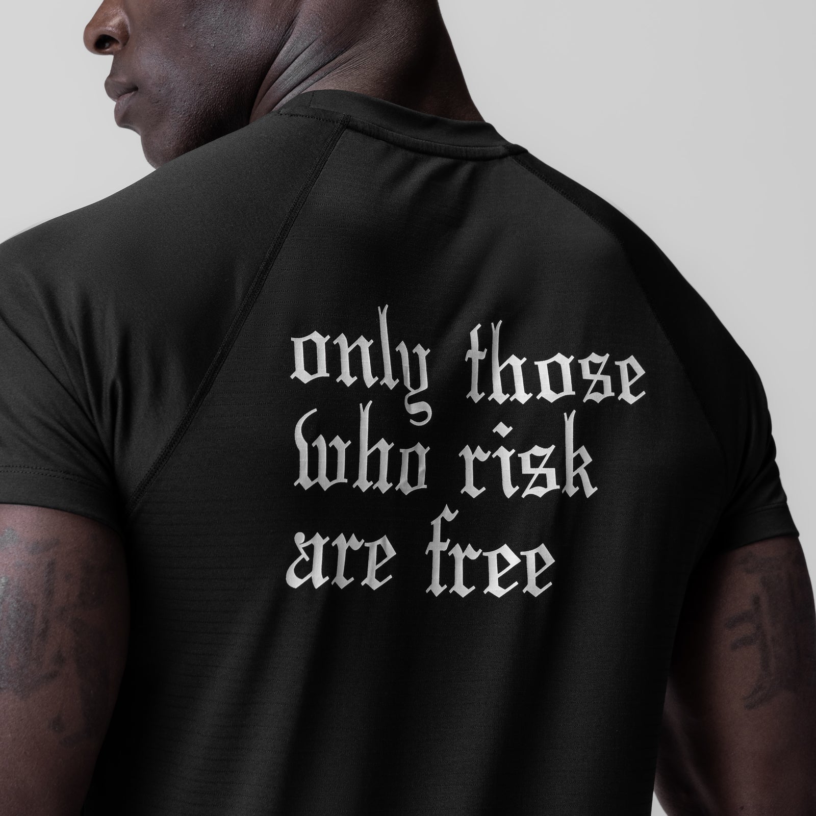 Black fitted tee with 'only those who risk are free' text, worn by model in profile view