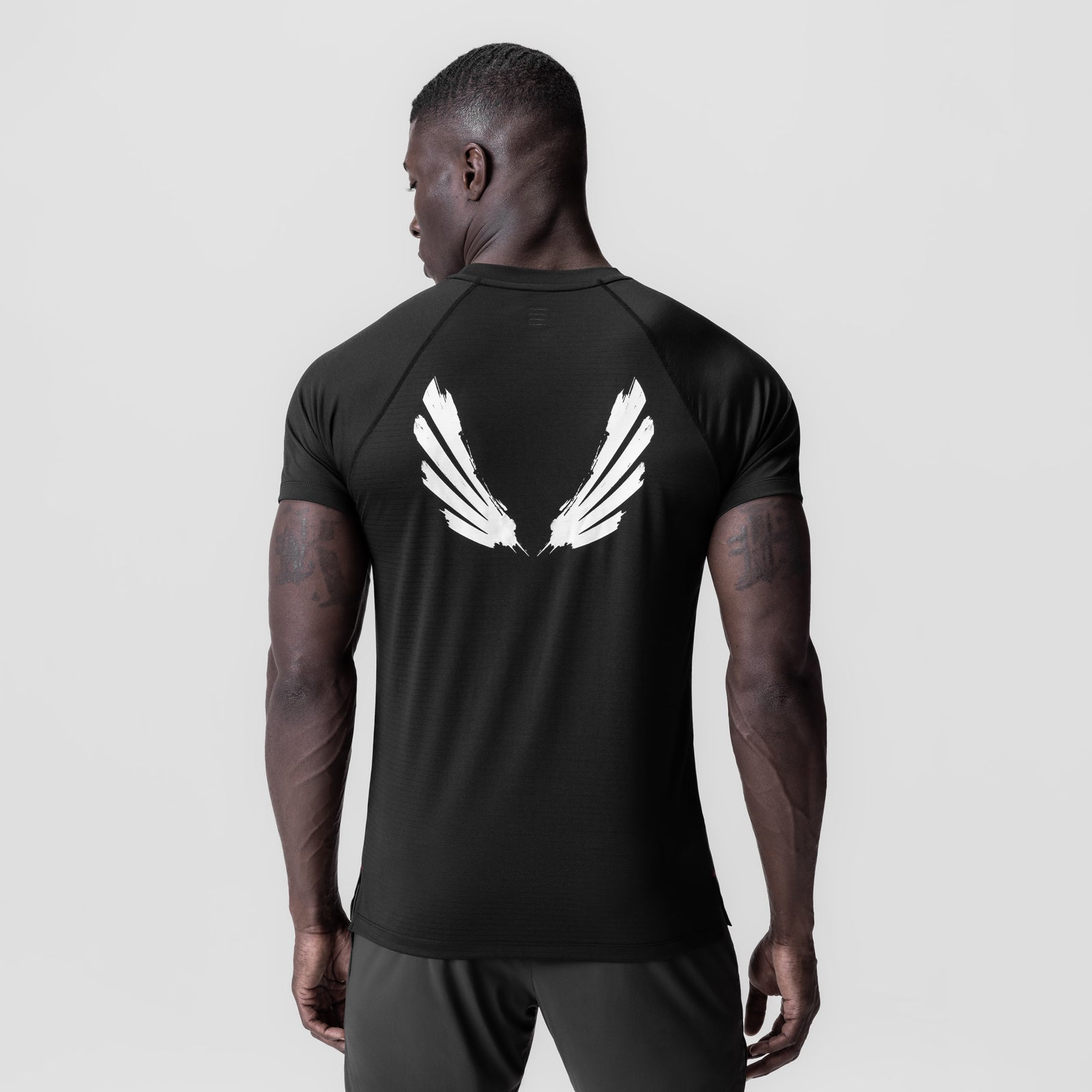 Black fitted tee with white brush wings graphic on back, worn by model