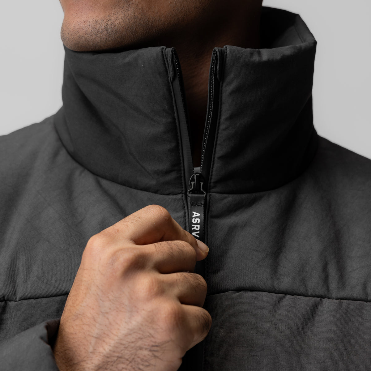 Black PrimaLoft puffer jacket on model, detail of full-length zipper and high collar