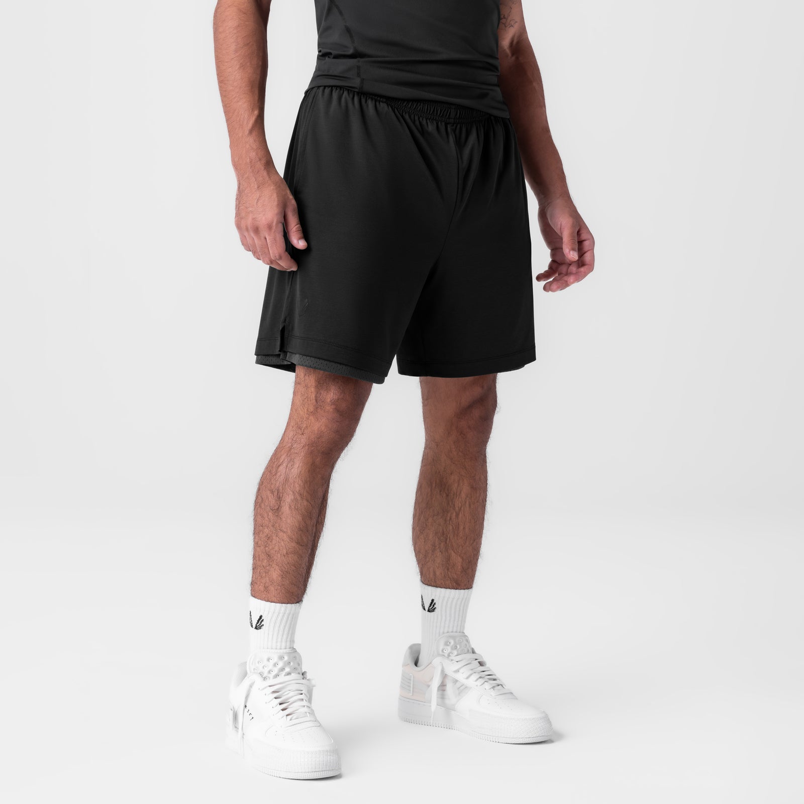 Black reversible 2-in-1 shorts worn by model with white sneakers and white socks, side view