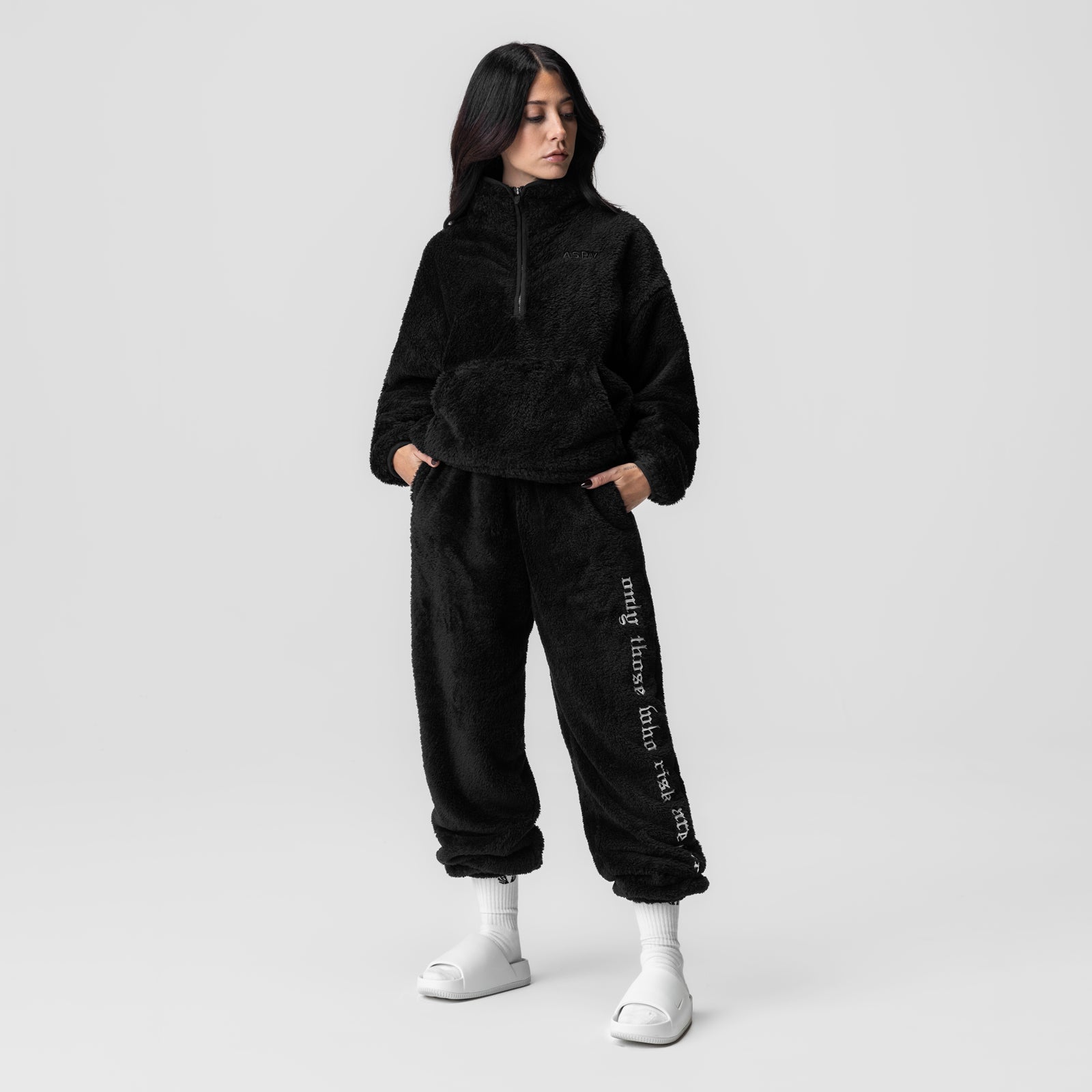 Black sherpa joggers with white text on leg, worn with matching black half-zip pullover and white socks