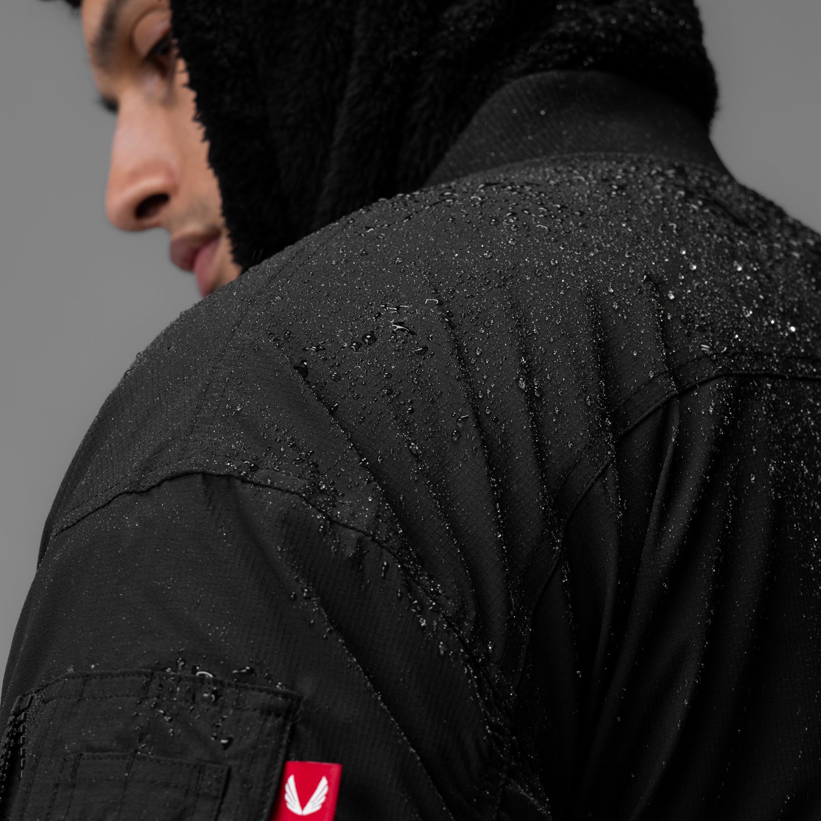 Black sherpa-lined insulated bomber jacket worn by model, back view, wet from rain