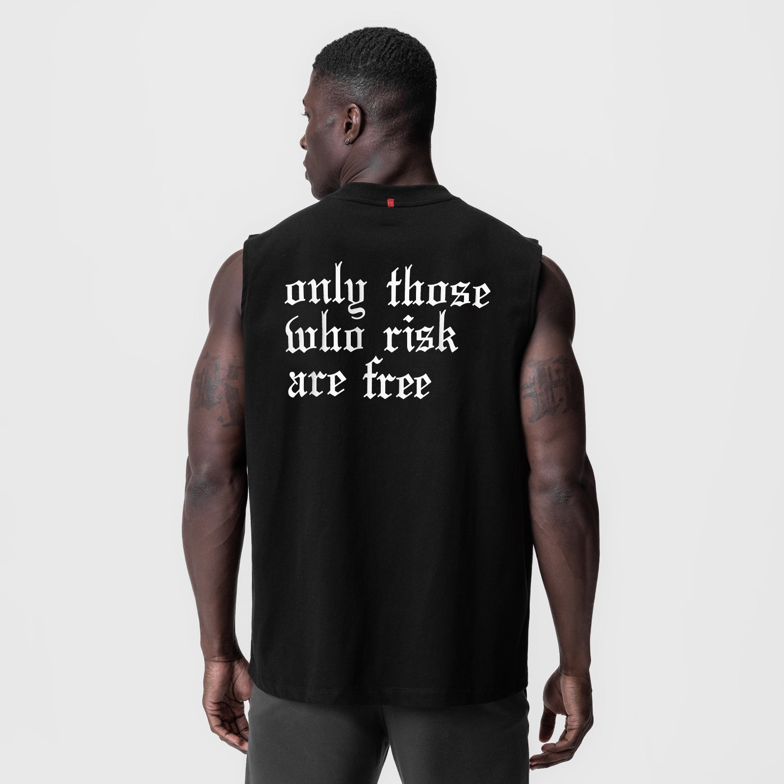 Black Tech Essential Relaxed Cutoff tank top with white 'only those who risk are free' text, back view on model