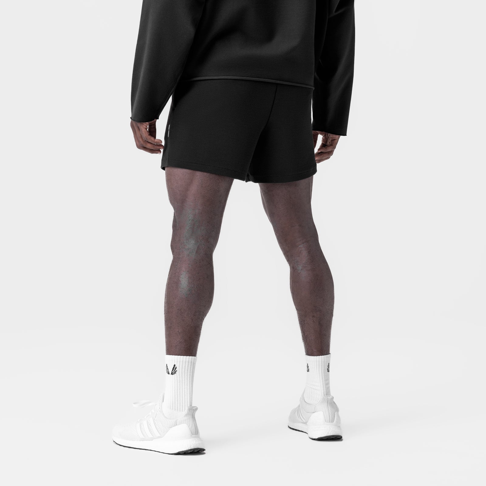 Black waffle knit sweat shorts worn with white socks and sneakers, back view