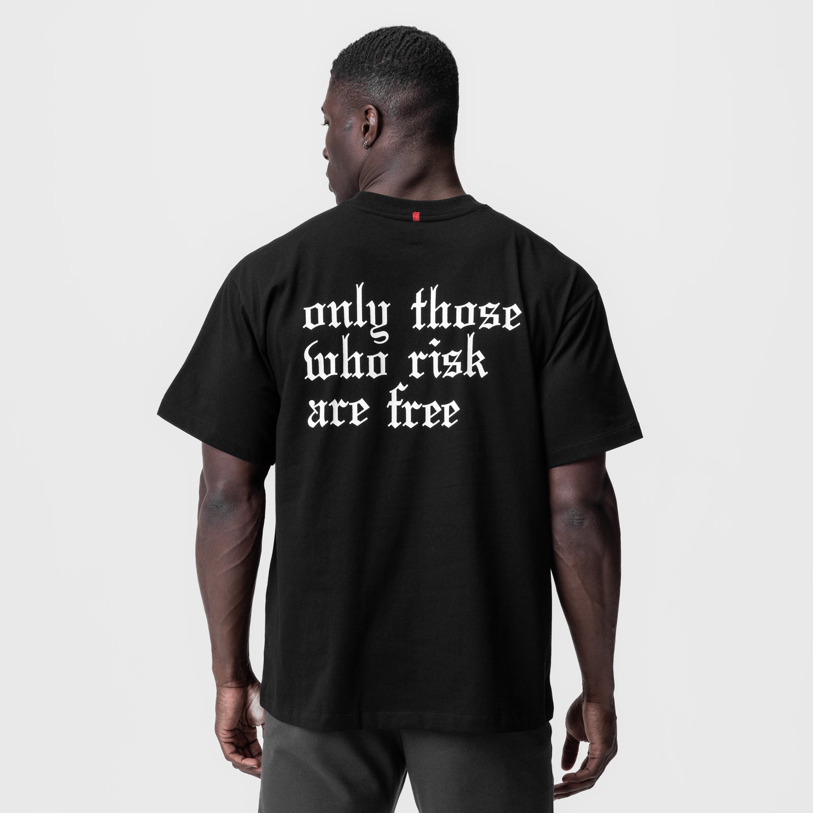Black Tech Essential Relaxed Tee with 'only those who risk are free' text, back view on model