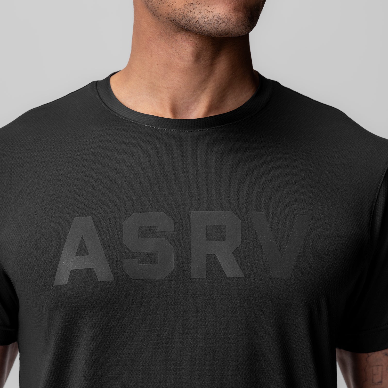 Black ASRV Essential Tee worn by male model, front view showing tonal ASRV logo